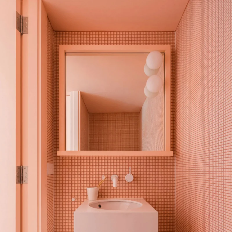 Tribe Studio applied coral pink to the tiled walls, under-sink storage cabinet, and mirror frame of this bathroom in a Sydney home.