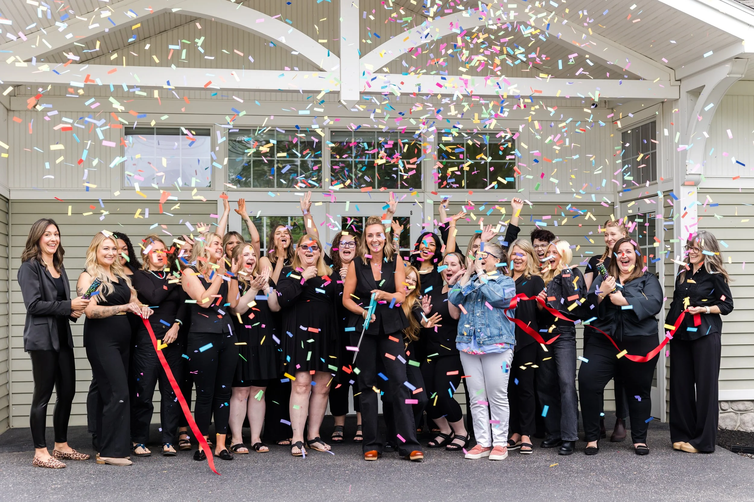 Group of women celebrating with confetti outside a building with white siding and large windows.