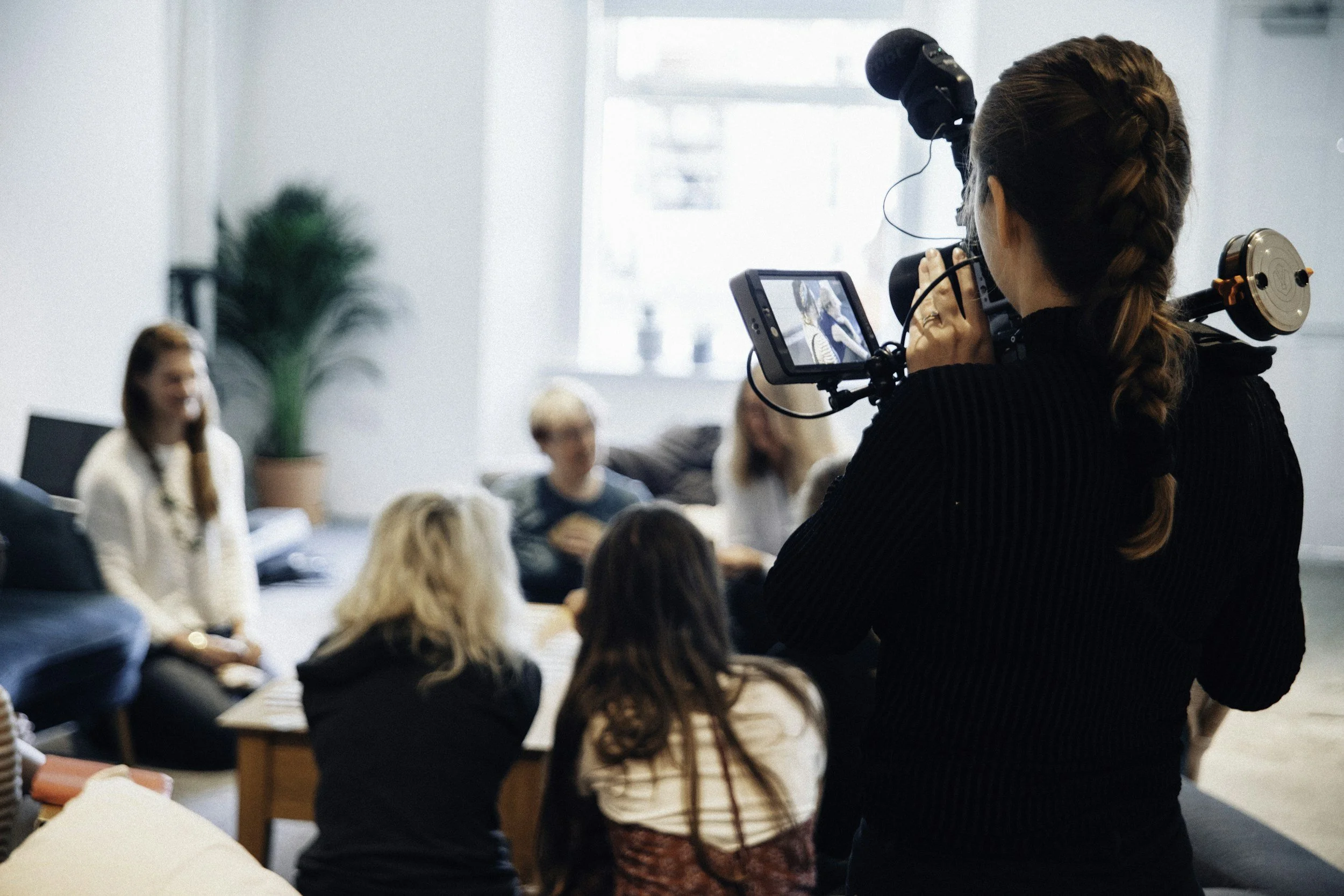 Image of a woman with a professional video camera recording people in a group setting discussing effects of the Temple Massager