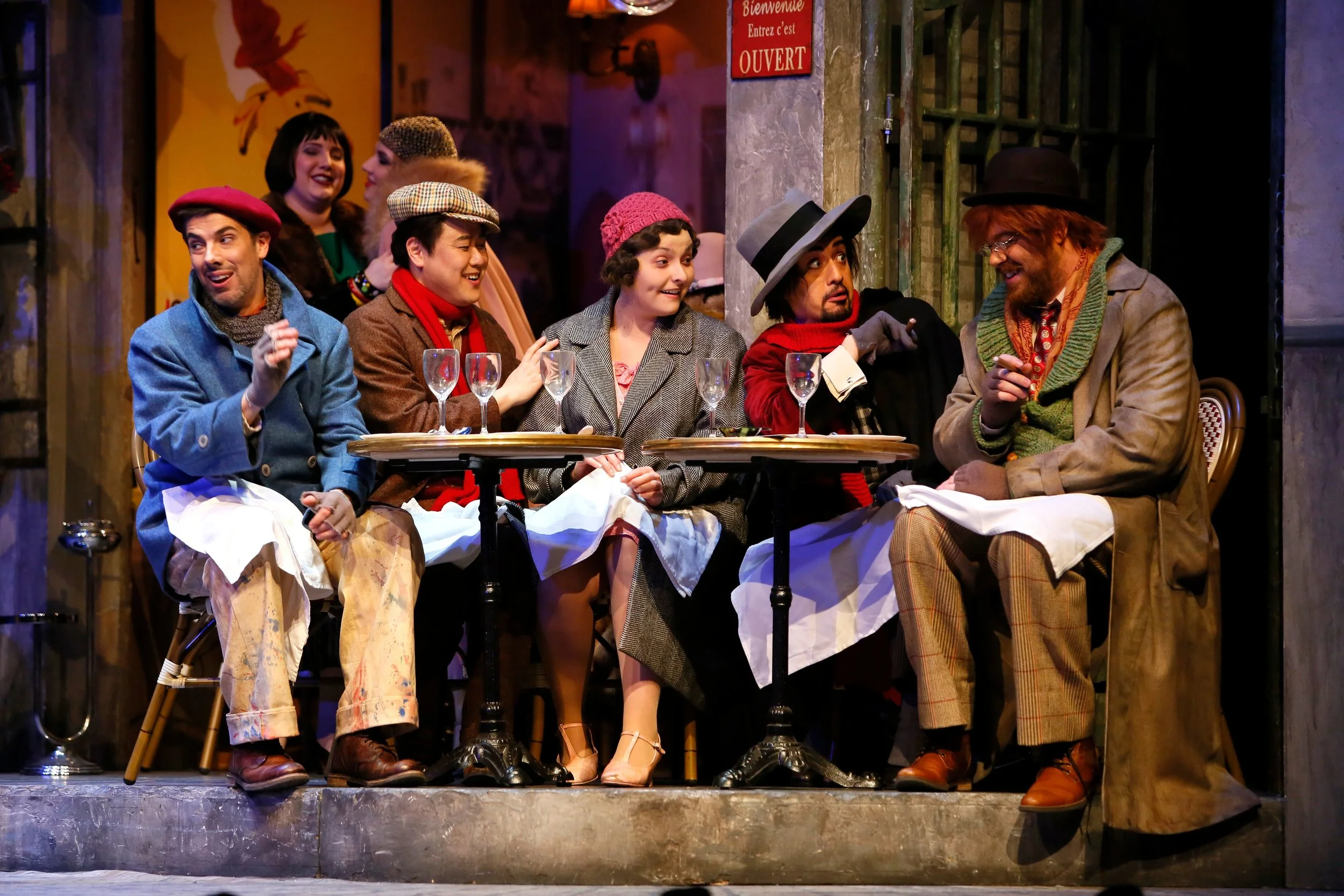 The story’s Bohemian friends enjoy Christmas eve at a Parisian cafe. Photo credit: Tim Matheson.