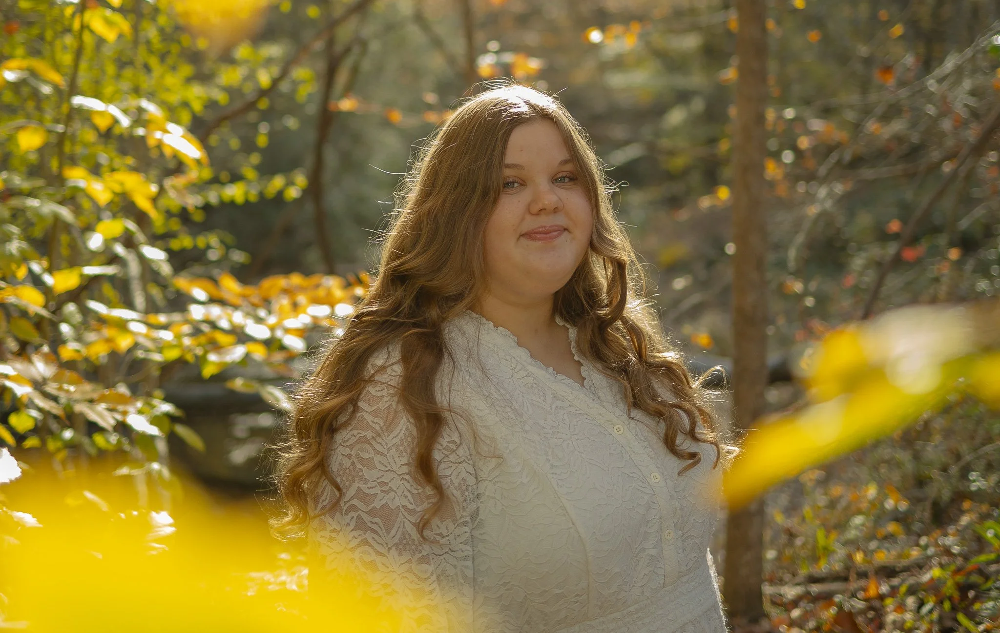 Cinematic portrait of a woman in a white dress, rim-lit by golden hour sun in a wooded environment.