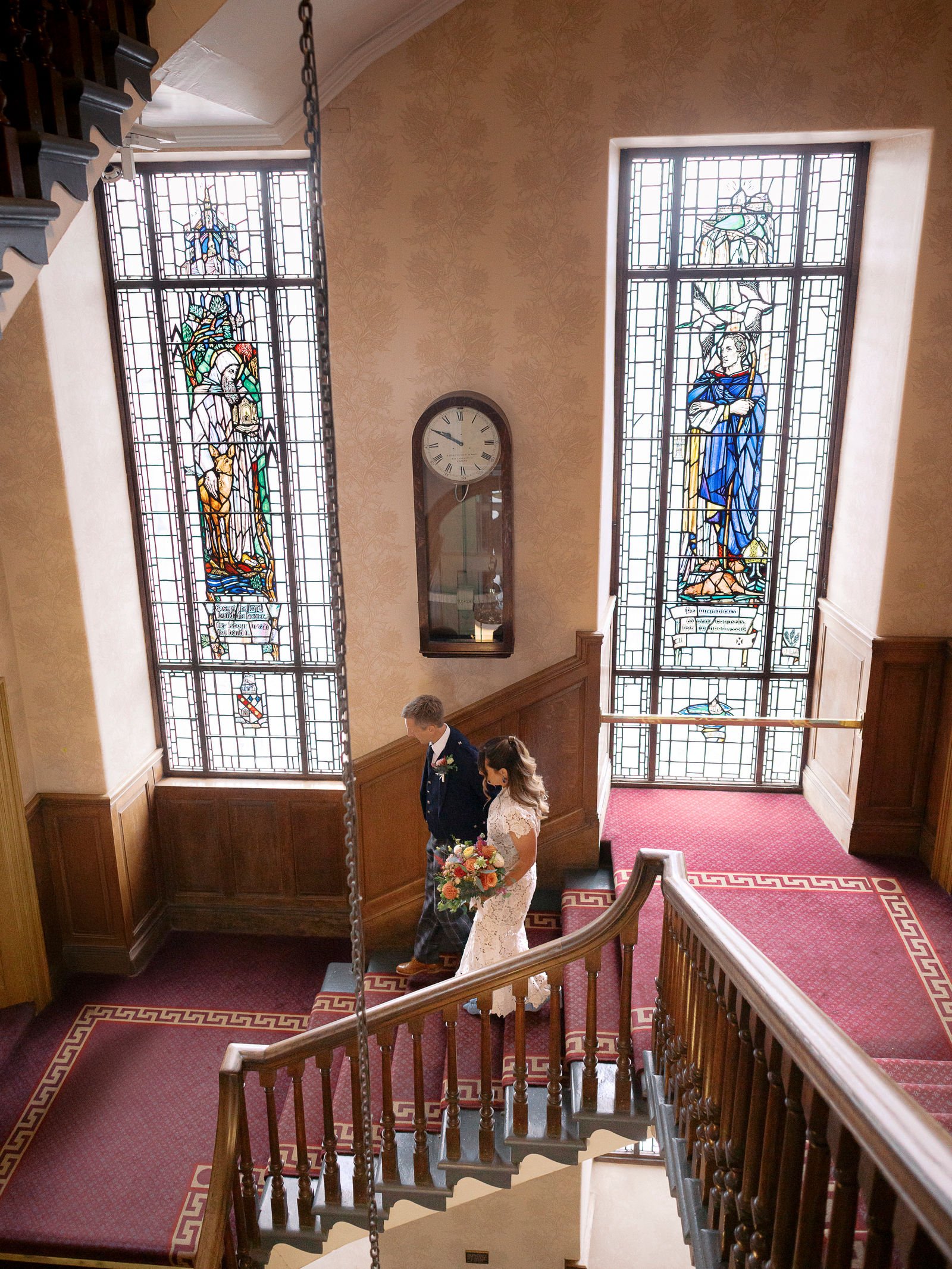 bride and groom walking down the stairs with stained glass windows at edinburgh city chambers