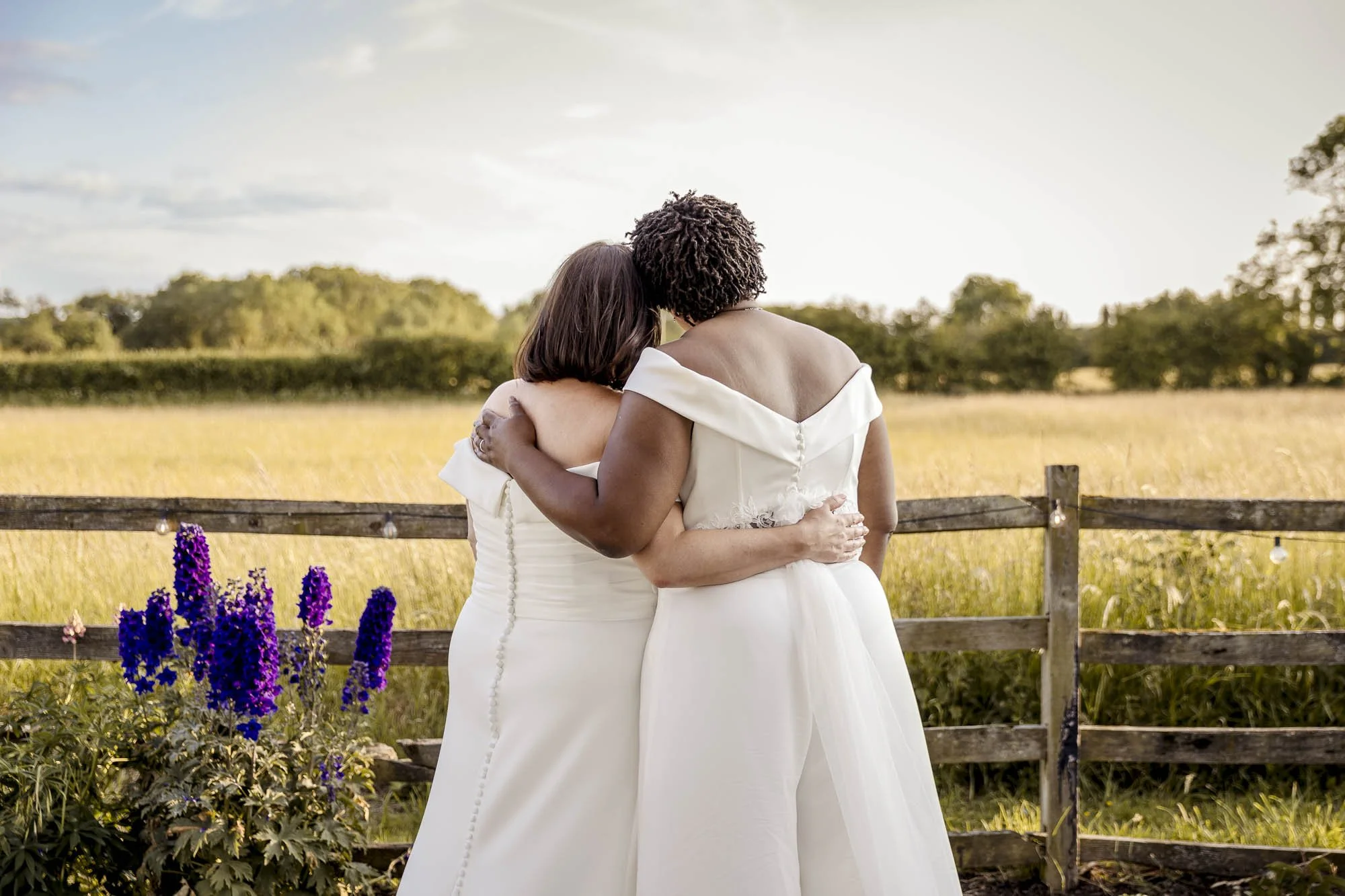 Brides in white embrace amongst the flowers before the rolling Leicestershire countryside at Badgers Mount Hotel Elmsthorpe