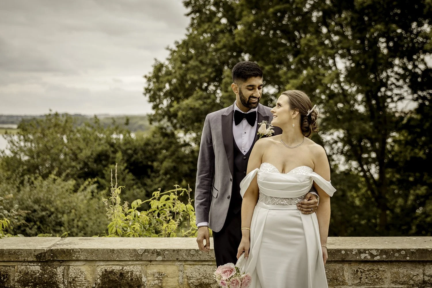 A bride and groom look at each other in the grounds of Rutland Hall with stunning countryside and lake views