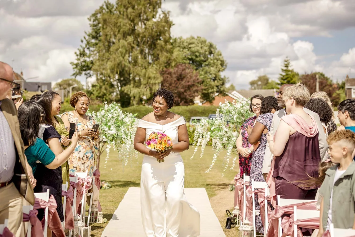 A bride walks the aisle whilst greeting and waving to her guests