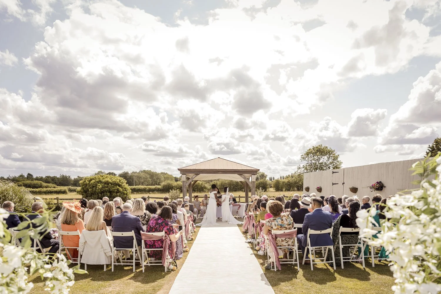 Two brides under a wooden pagoda at their outdoor wedding ceremony in Elmsthorpe Leicestershire