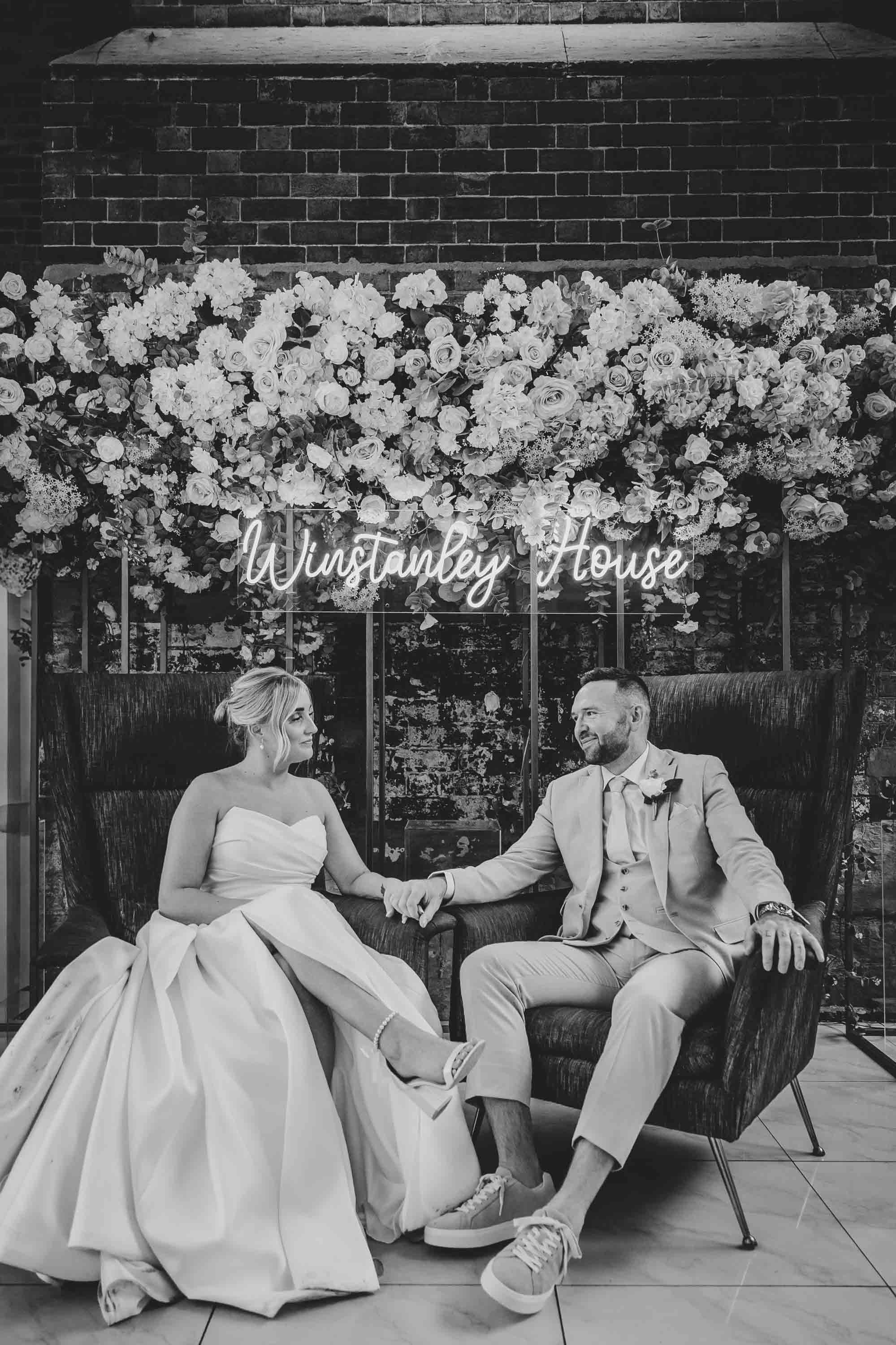 Bride and groom on comfy chairs under the sign at Winstanley House in Leicester