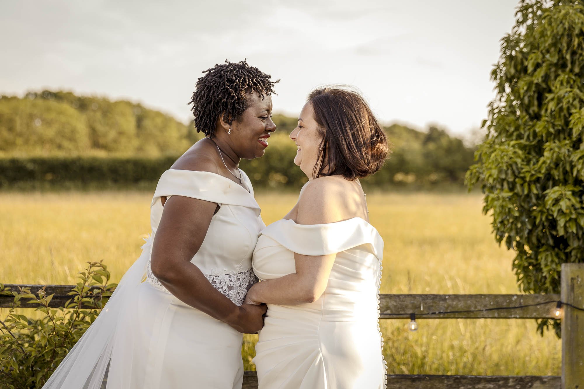 Two brides in white enjoy a private moment within a countryside backdrop at Badgers Mount in Leicestershire