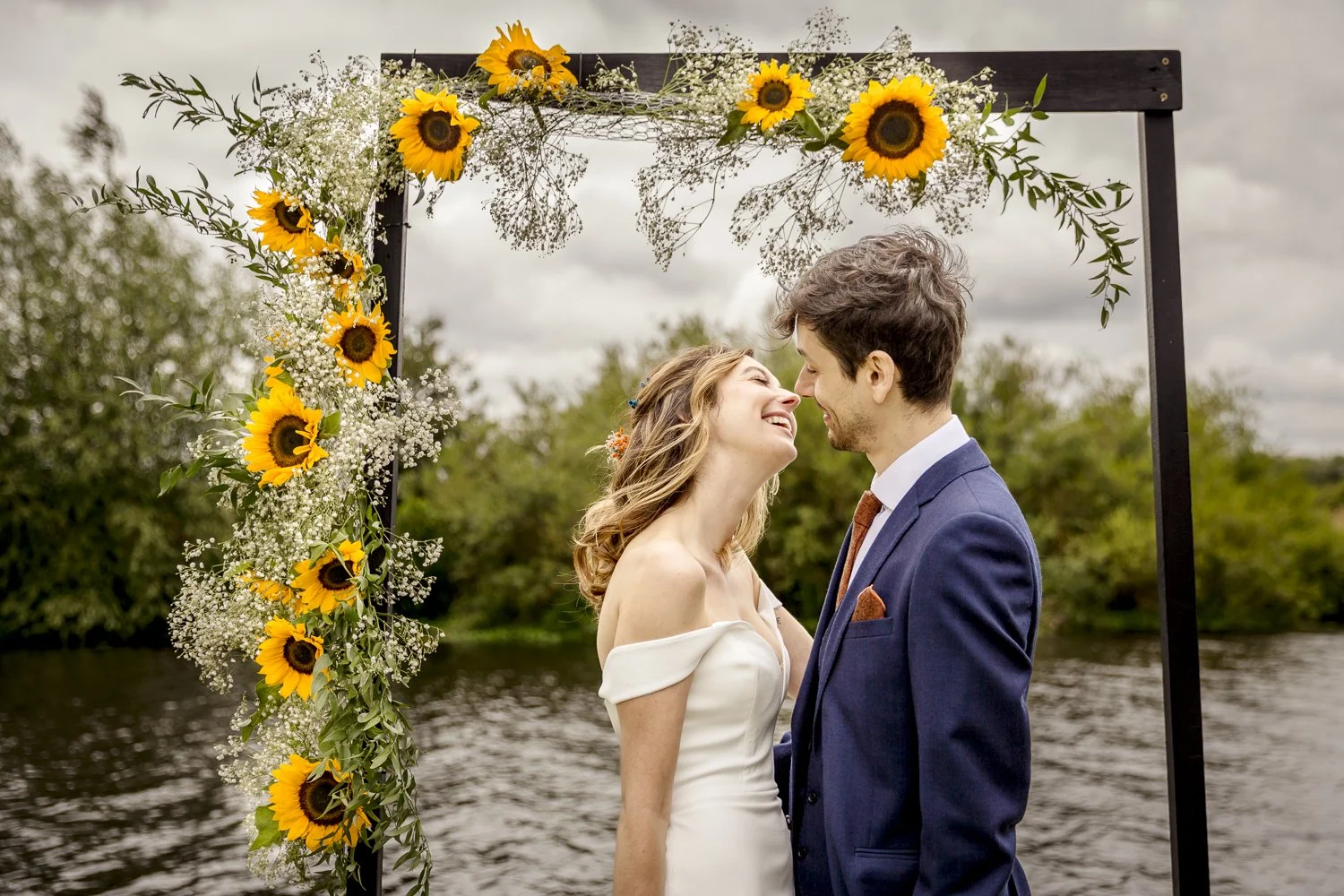 Natural moment of a couple before they kiss after their wedding ceremony. They stand beneath a wooden frame surrounded by big yellow sunflowers