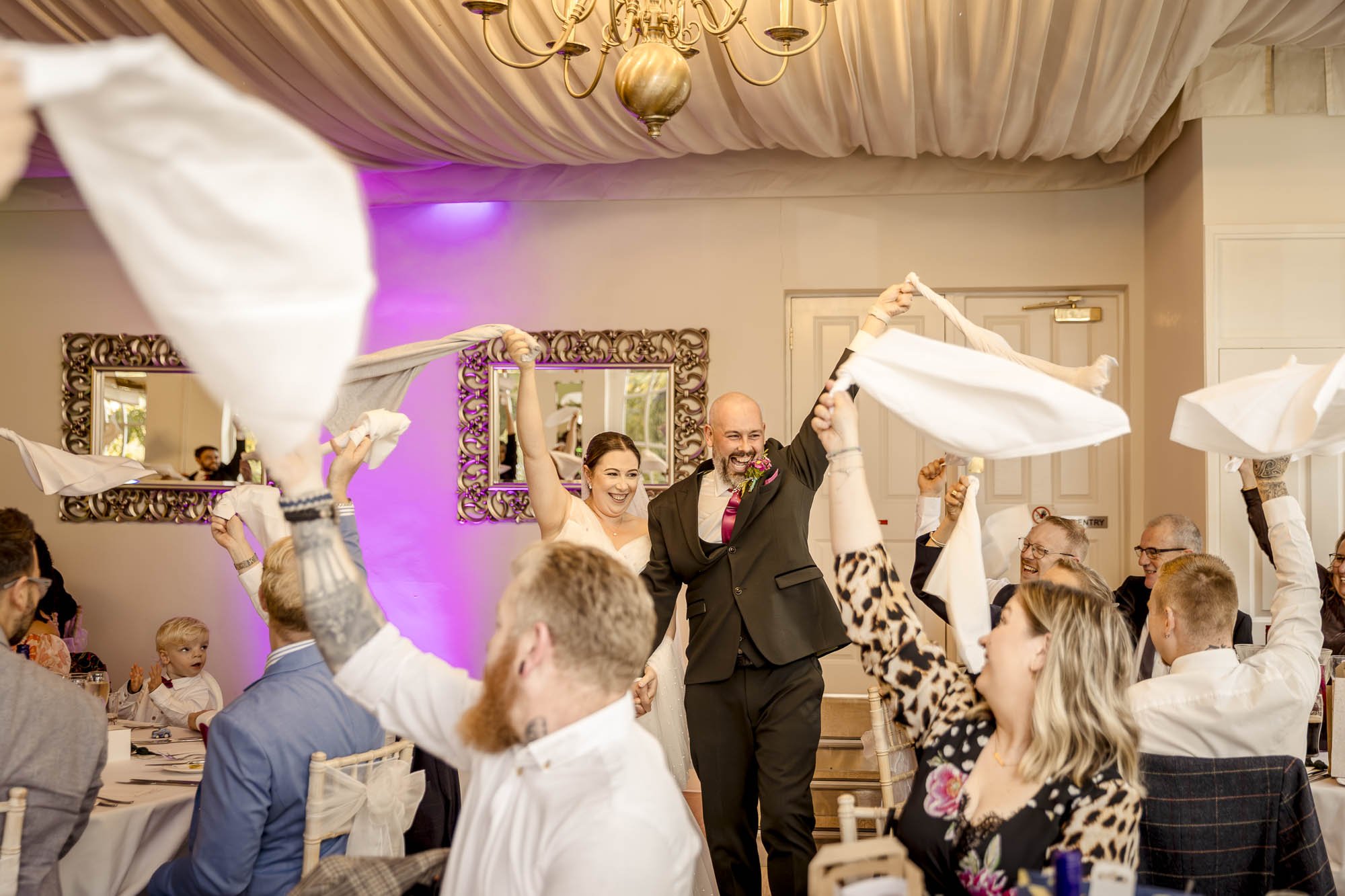 Bride and groom enter the wedding breakfast to their favourite song whilst their guests laugh and twirls their table napkins