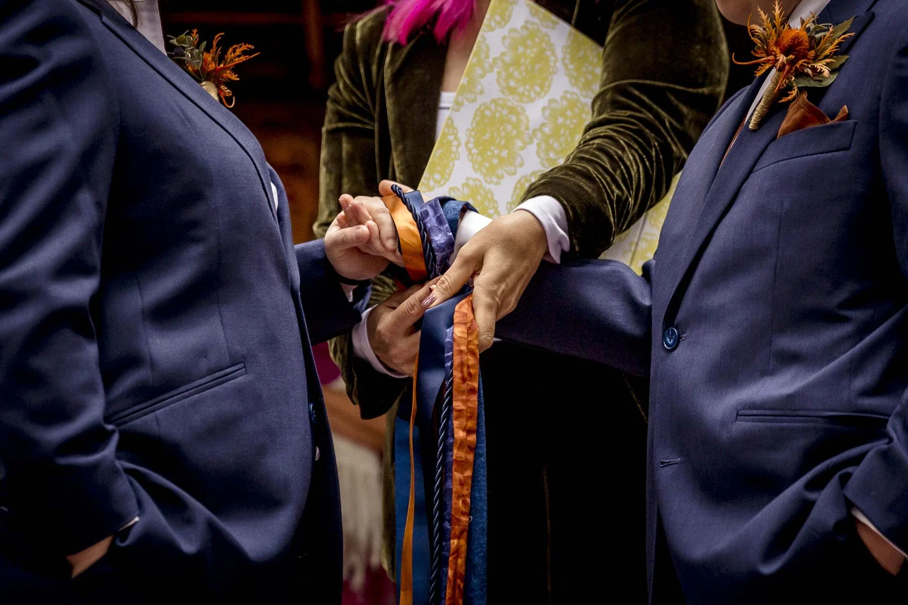 Celebrant performing a hand fasting ceremony with navy and burnt orange ropes and ribbons