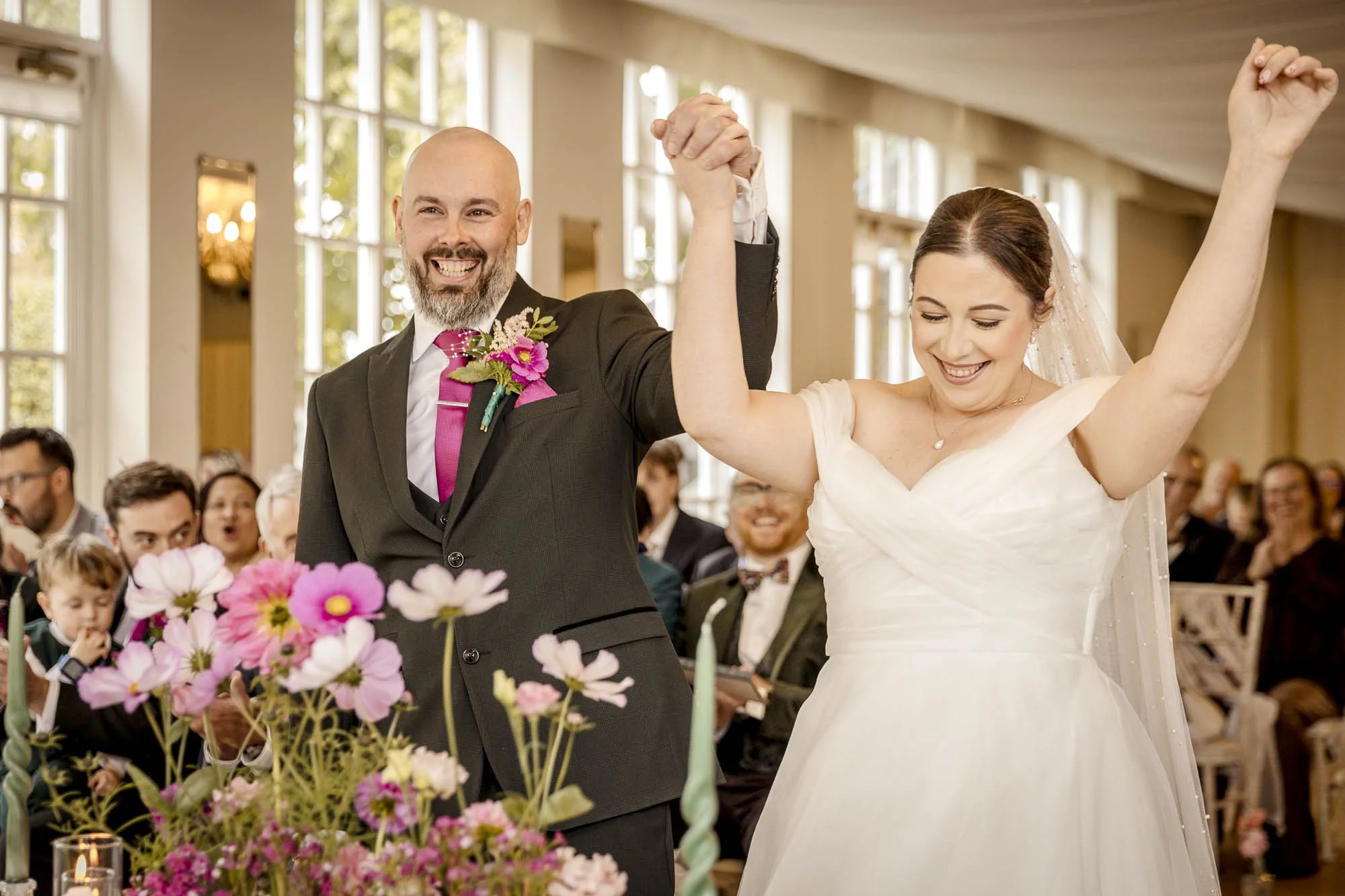 A bride and groom playfully dance in their wedding ceremony at Warwick House Warwickshire whilst their guests laugh and cheer