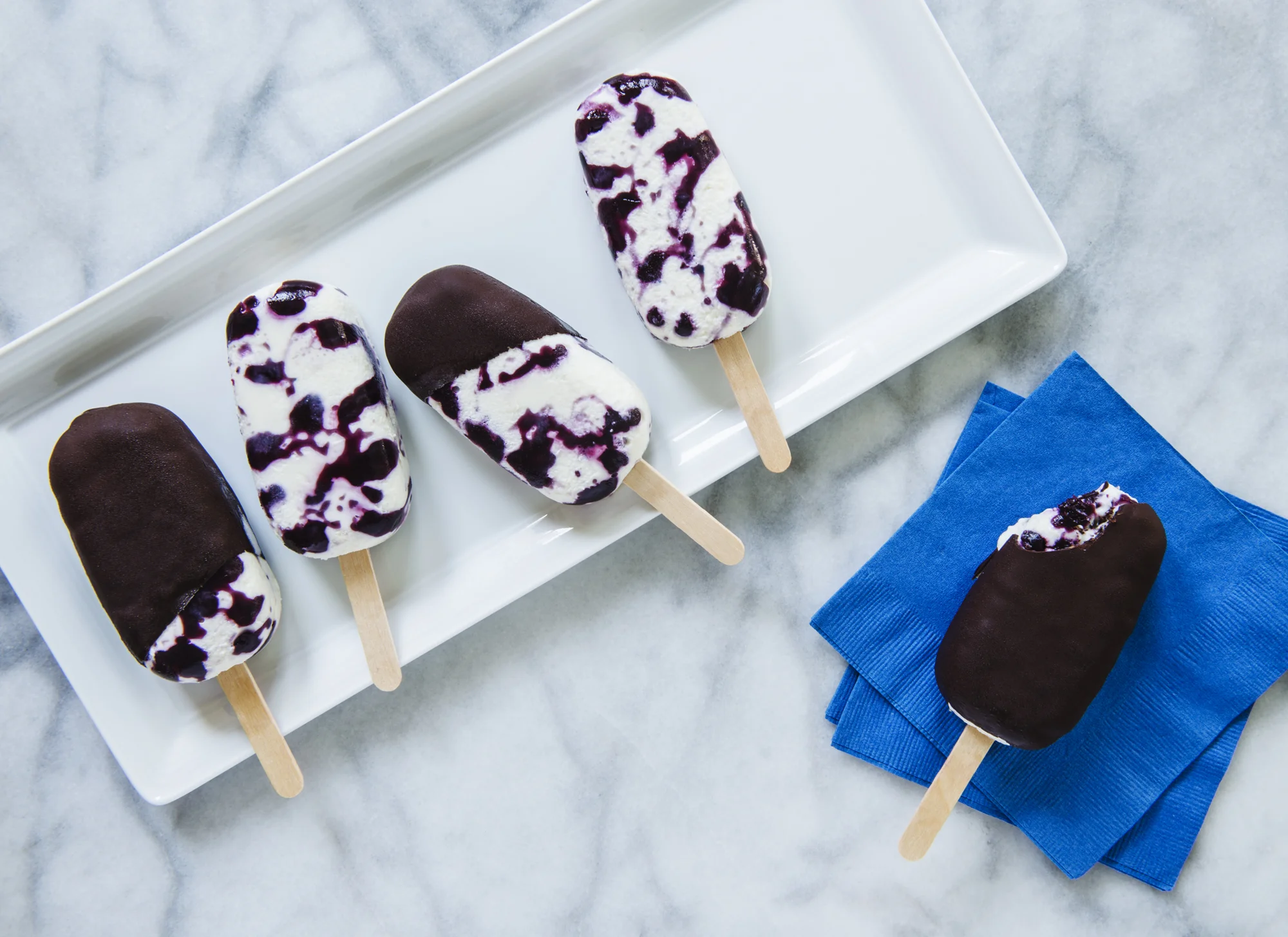 Photos by Michael Marquand Recipes by Marilinda Hodgdon Nothing speaks of summer in Maine like wild blueberries. These berry beauties combined with creamy cheesecake ice cream, crafted into popsicles dipped in dark chocolate, spell a fabulous finish to a sumptuous summer picnic supper. The Magic of the chocolate sauce is that it hardens onto the cold ice cream almost instantly. The recipe is one of the most simple and easy chocolate sauces imaginable. This tasty treat will delight at first bite. My memorable recipe for Maine Blueberry Cheesecake Ice Cream Popsicles makes about 12 popsicles. Use horizontal silicon molds with holes for the sticks. Make sure your sticks fit the mold openings. Most molds come with the appropriate sticks.