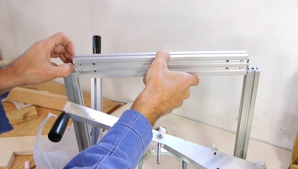 Then slide the cross piece into the uprights. The cross piece has two fasteners on each end for attaching to the rail. You may need to use a screwdriver to lightly push them outwards as you slide the crosspiece in. You may also need to loosen the screws holding these fasteners to get them in.