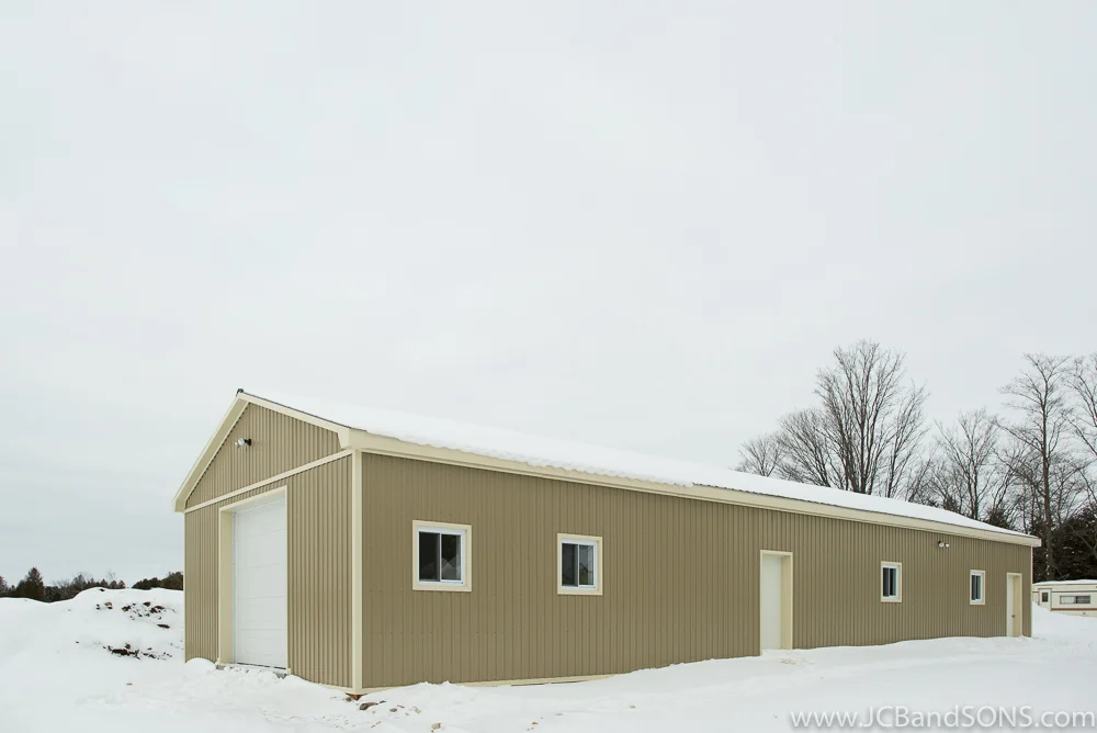 Completed honey shed exterior near Holstein with coffee-colored metal siding, light trim accents, and new steel roof, designed for both pool storage and apiary work.