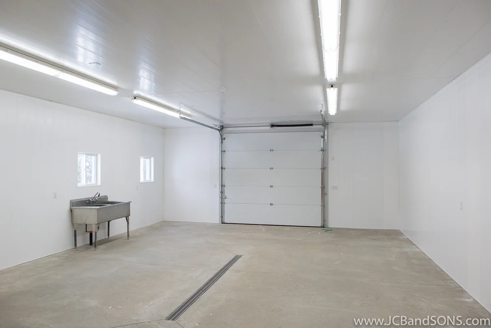 Completed honey extraction building near Durham featuring washable vinyl paneling, center floor drain, and large overhead door for equipment access.
