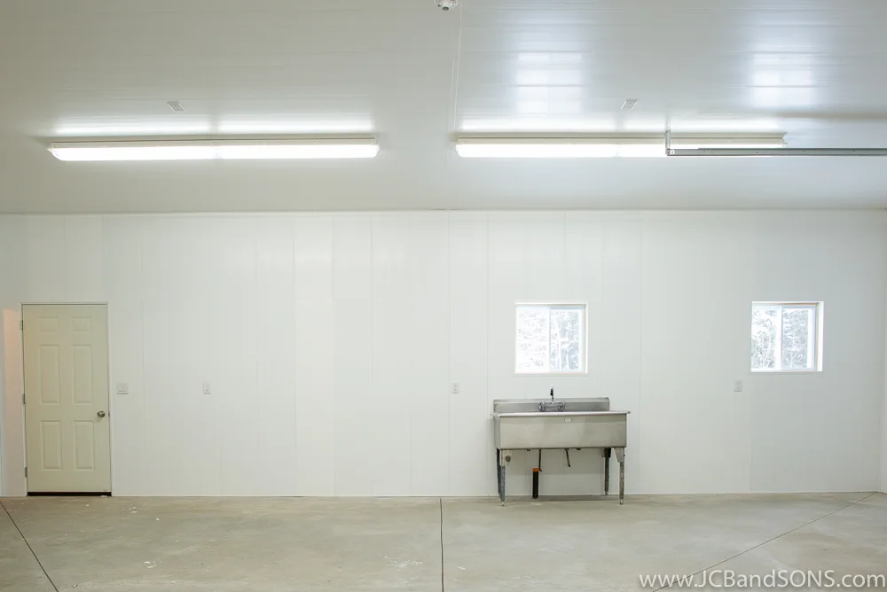 Completed interior of Southgate honey extraction room showing stainless steel sink, Trusscore wall and ceiling panels, concrete floor, and LED lighting.