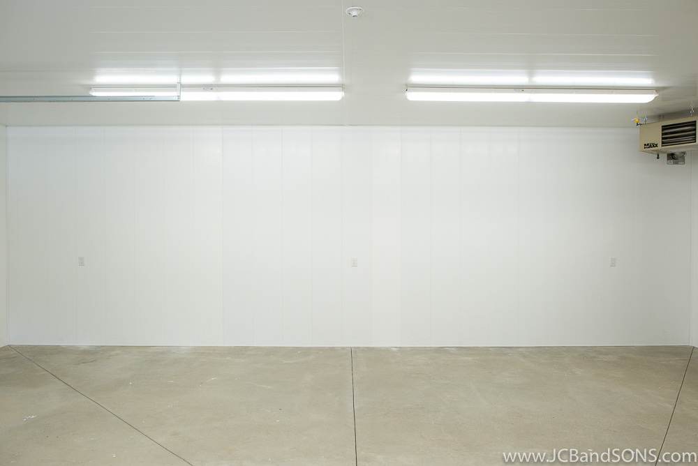 Honey extraction room in Southgate showing Trusscore walls, LED lighting, ceiling-mounted propane heater, and smooth concrete flooring.