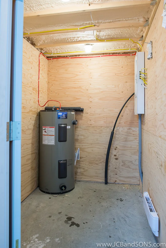Utility room in Southgate honey shed showing hot water tank, electrical panel, water line entry, and plywood-lined walls for durability.