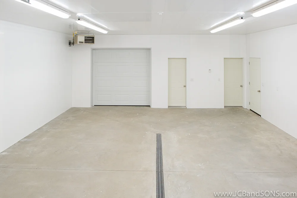 Completed interior of Southgate honey shed showing Trusscore walls and ceiling, overhead door to warehouse, utility room access, LED lighting, and center floor drain.