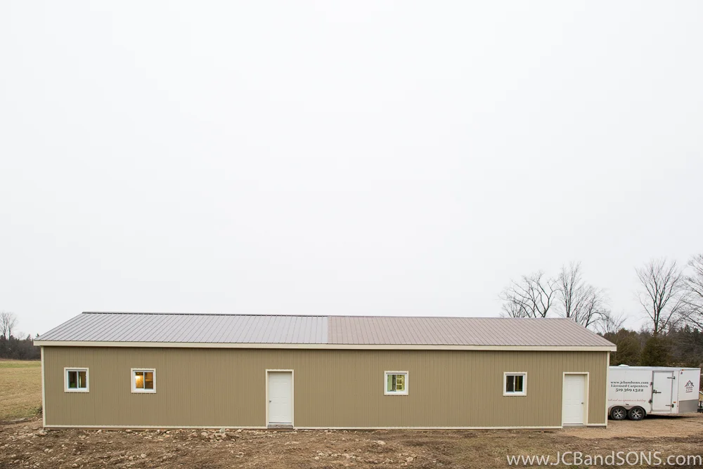 Completed honey shed exterior near Holstein with coffee-colored metal siding, light trim accents, and new steel roof, designed for both pool storage and apiary work.