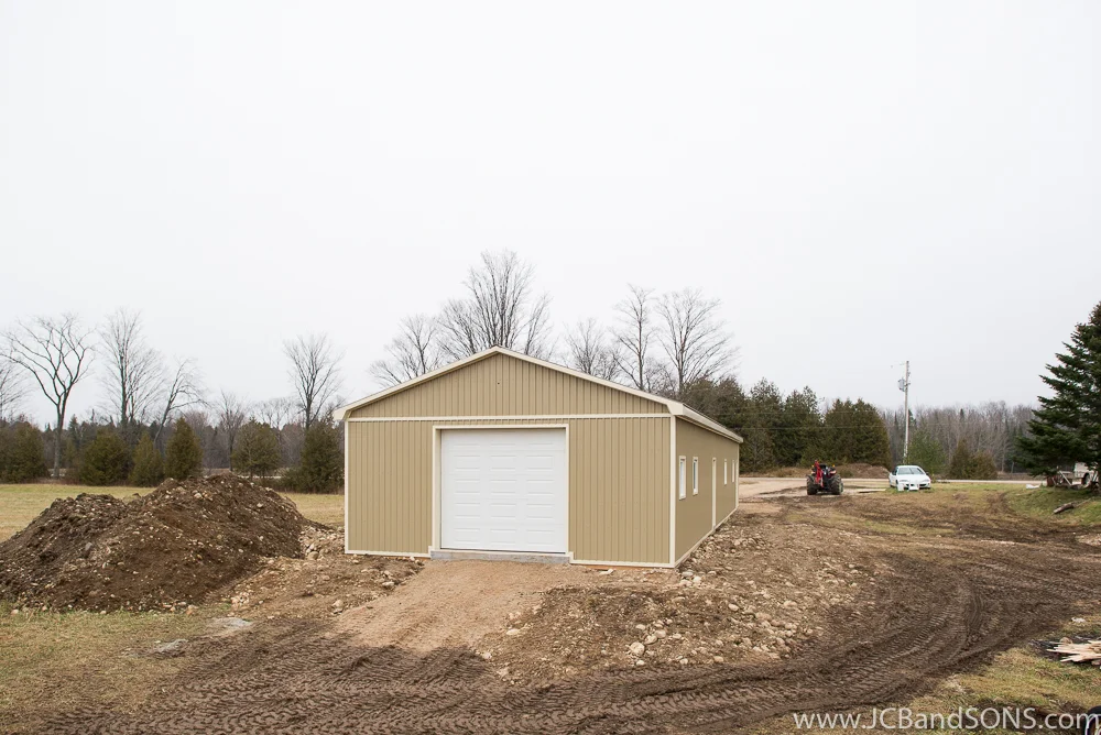 Completed front corner view of honey extraction building with two-tone steel siding and cream trim, constructed near Mount Forest for a local beekeeping operation.