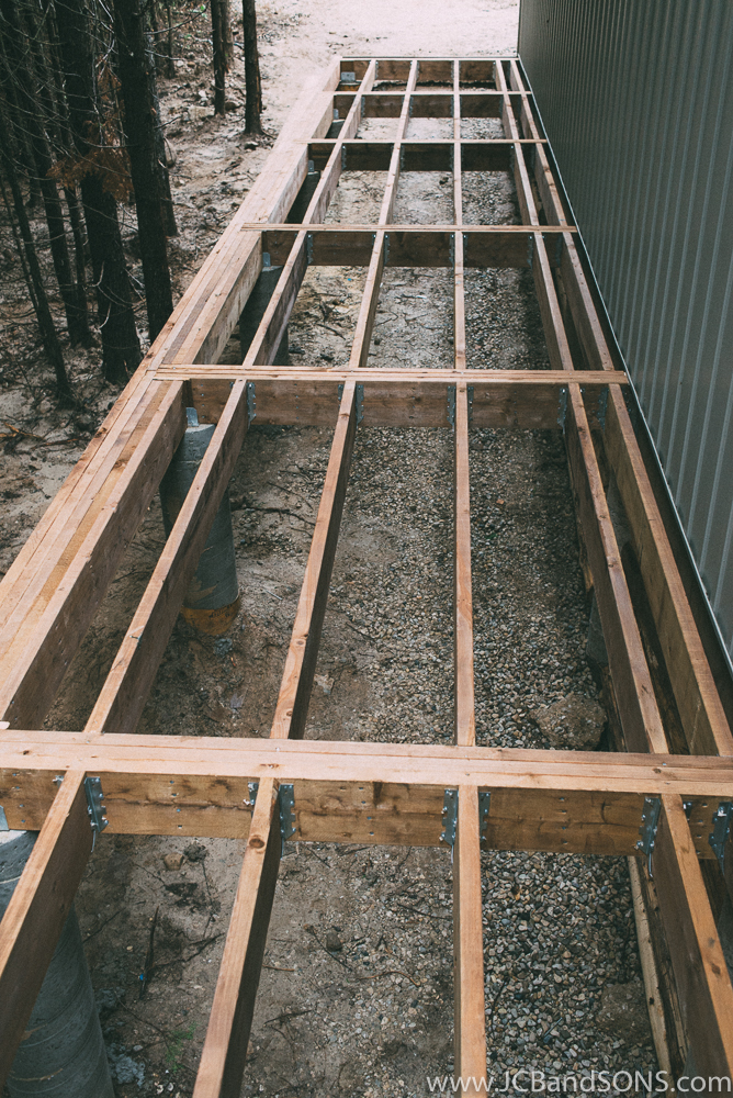 Galvanized joist hanger brackets were used with galvanized joist hanger nails to get flush beams keeping the framing off of the ground even at the lowest end.