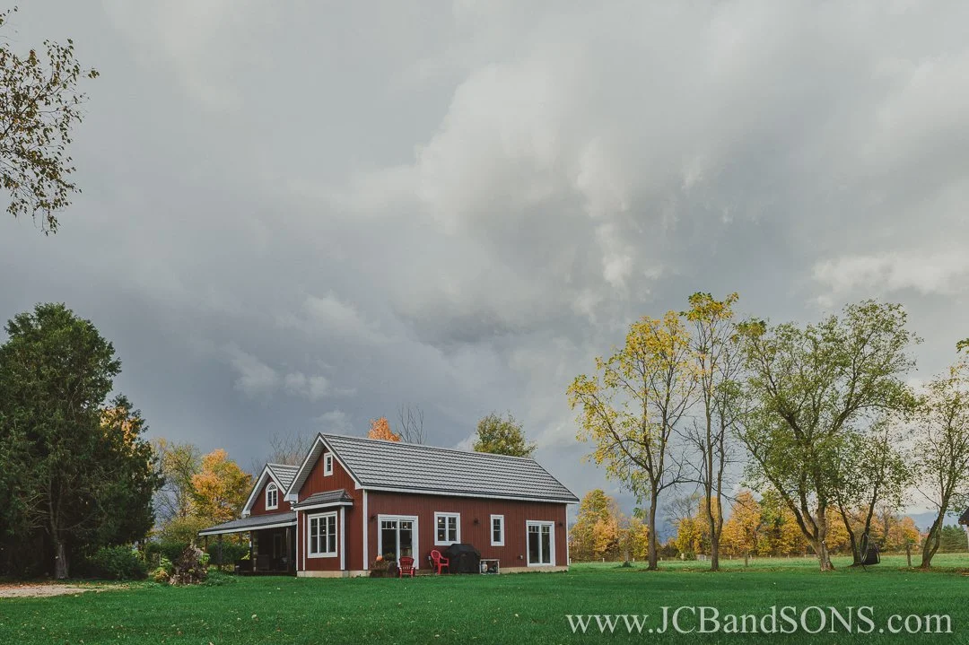 Completed heritage log home with new rear addition featuring red siding and energy-efficient white vinyl windows