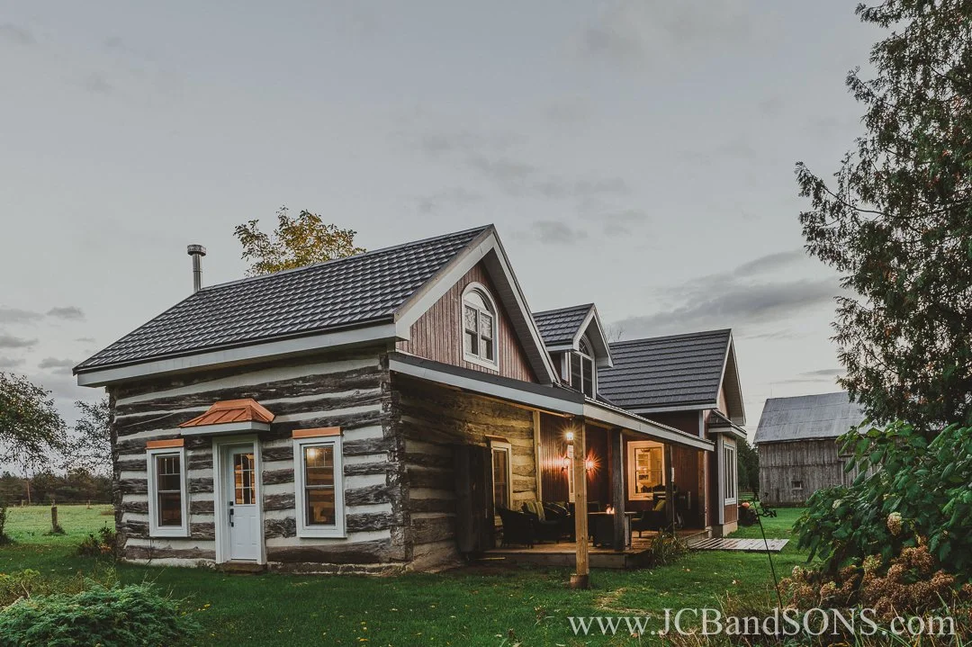 Evening glow on completed red siding and white-trimmed windows of completed heritage log home addition