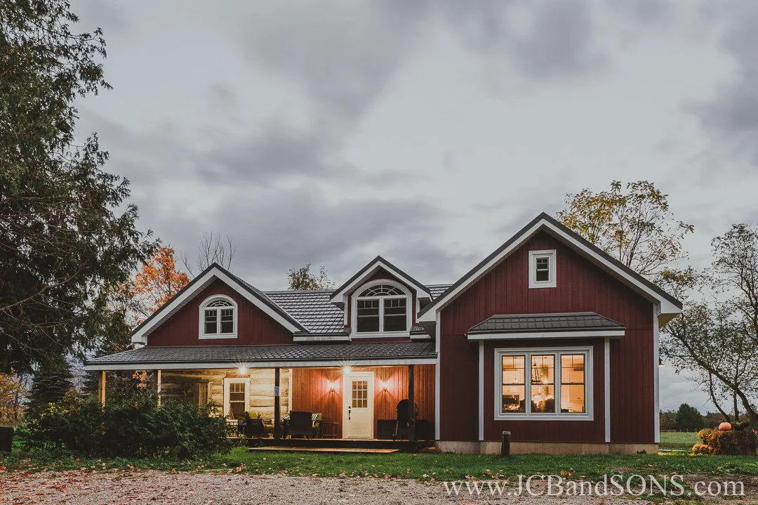 Completed log home addition with white vinyl windows and red siding, photographed at dusk with exterior lights on