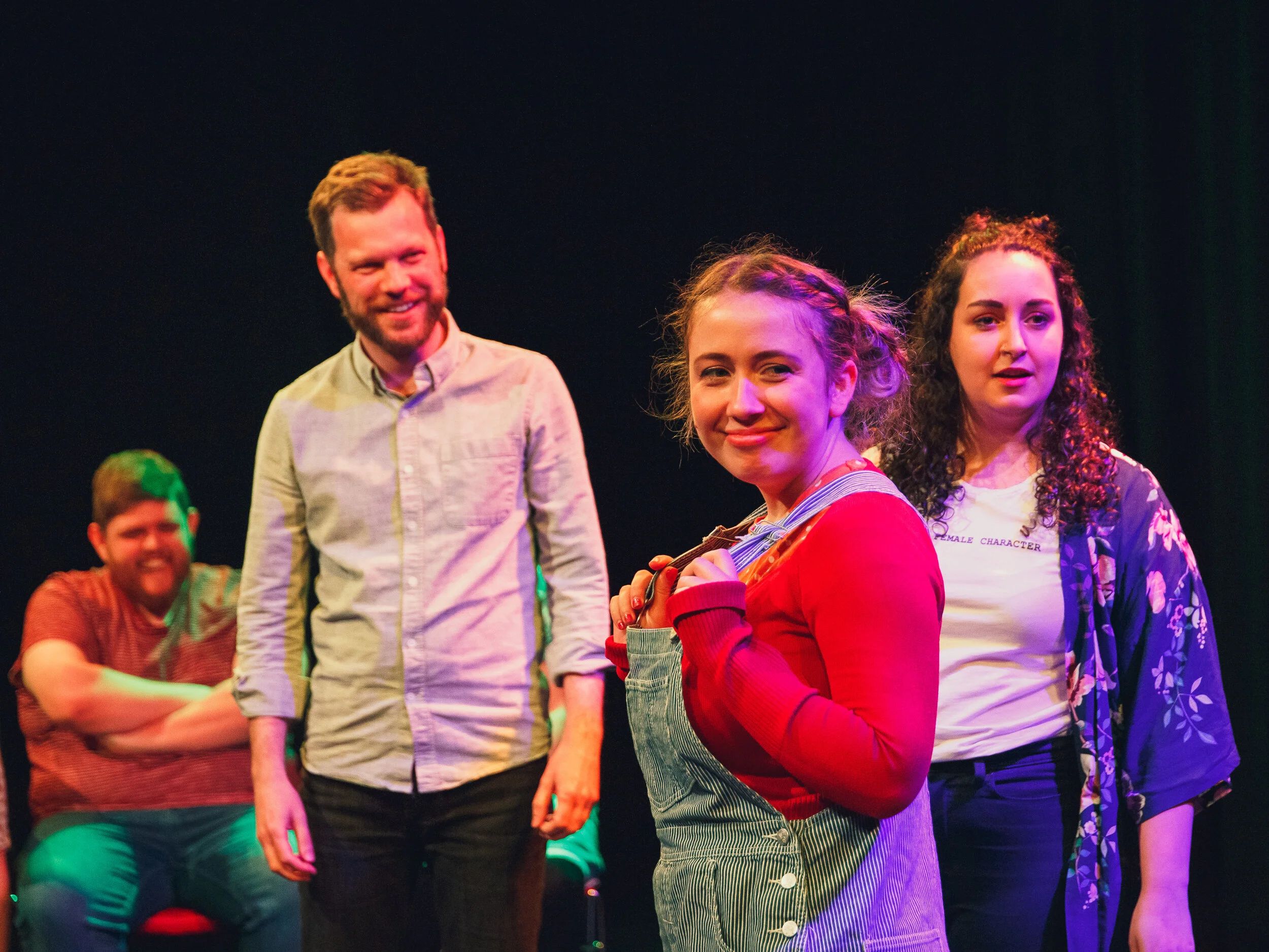 The Saboteur, photo by Alex Rabina  Image description: three improvisors standing, one sitting in the background, all smiling and looking cheeky. Everyone is looking off camera at the show host (not pictured)