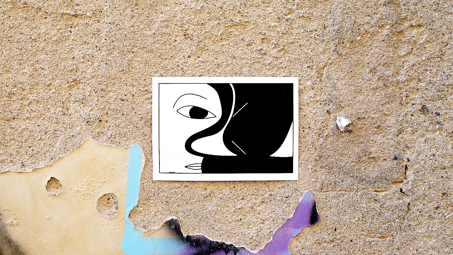 Black and white abstract artwork of a face with one eye, nose, and lips, arranged in a minimalist style, taped to a textured beige wall with peeling paint.