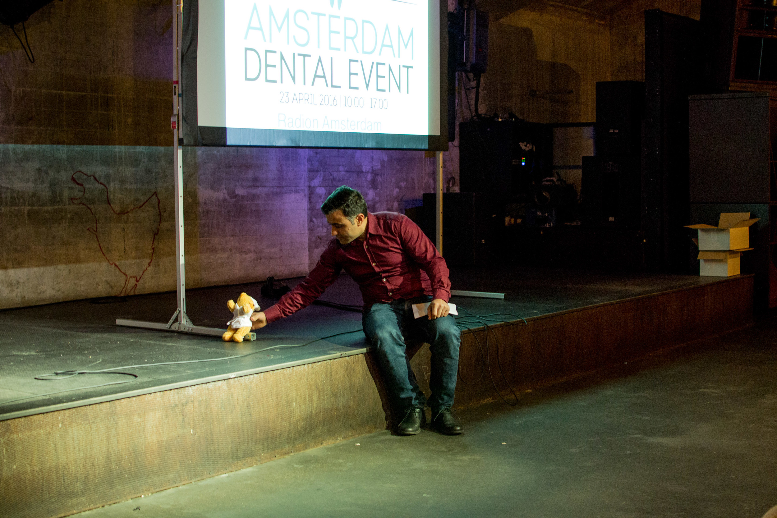 Dagvoorzitter Sinan Cihangir, die later op de dag voor lastige patiënt zal spelen, zet zijn zojuist gescoorde mascotte uit de EXPO Zaal - het beertje van Meeùs - klaar op het podium.