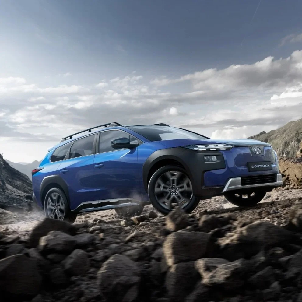 En blå Subaru Outback kjører på steinete terreng under en overskyet himmel.