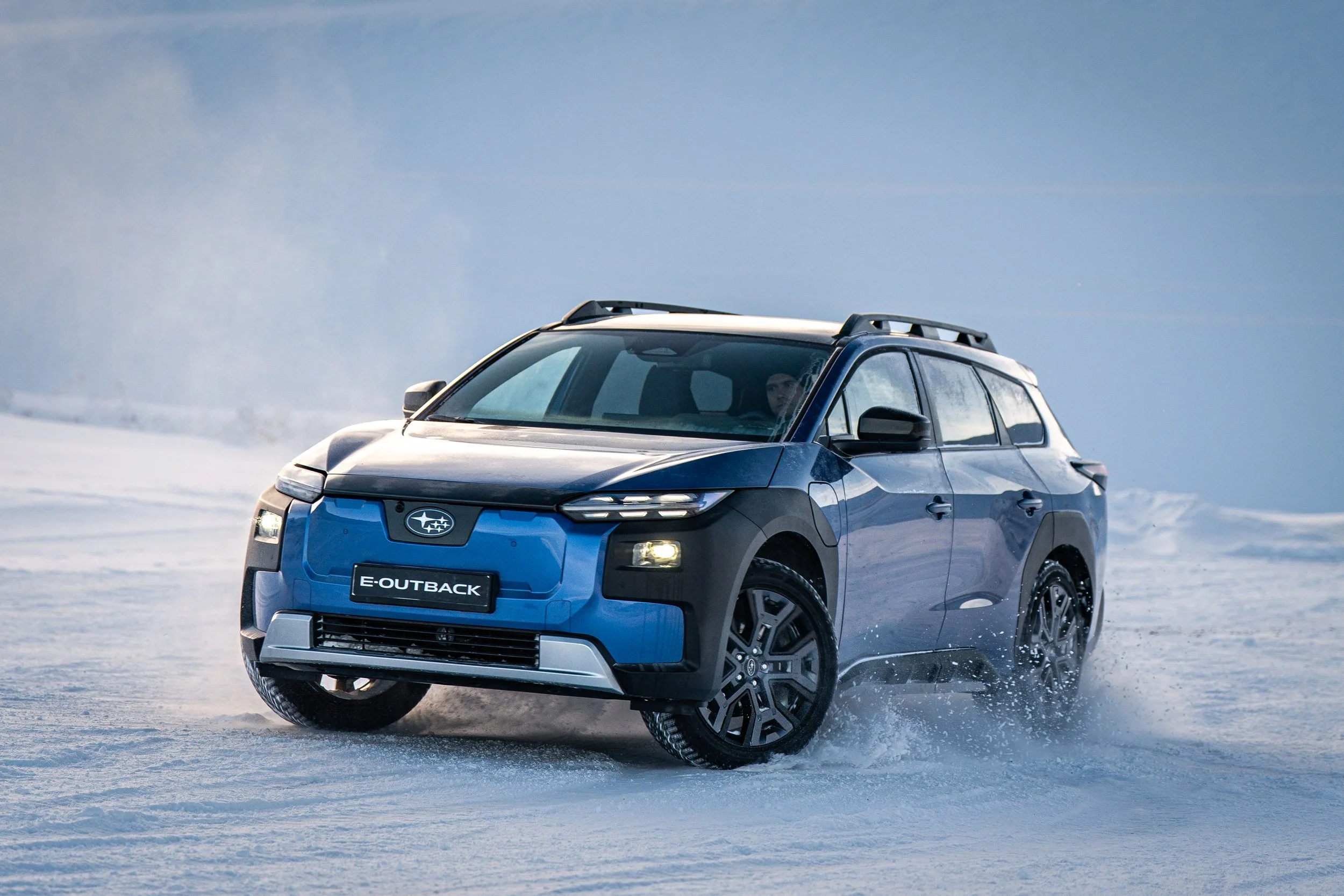En blå Subaru E-Outback kjører på snødekt terreng i kaldt vær. Aaland bil forhandler Subaru som nå har 10 års garanti og gode kampanjer!