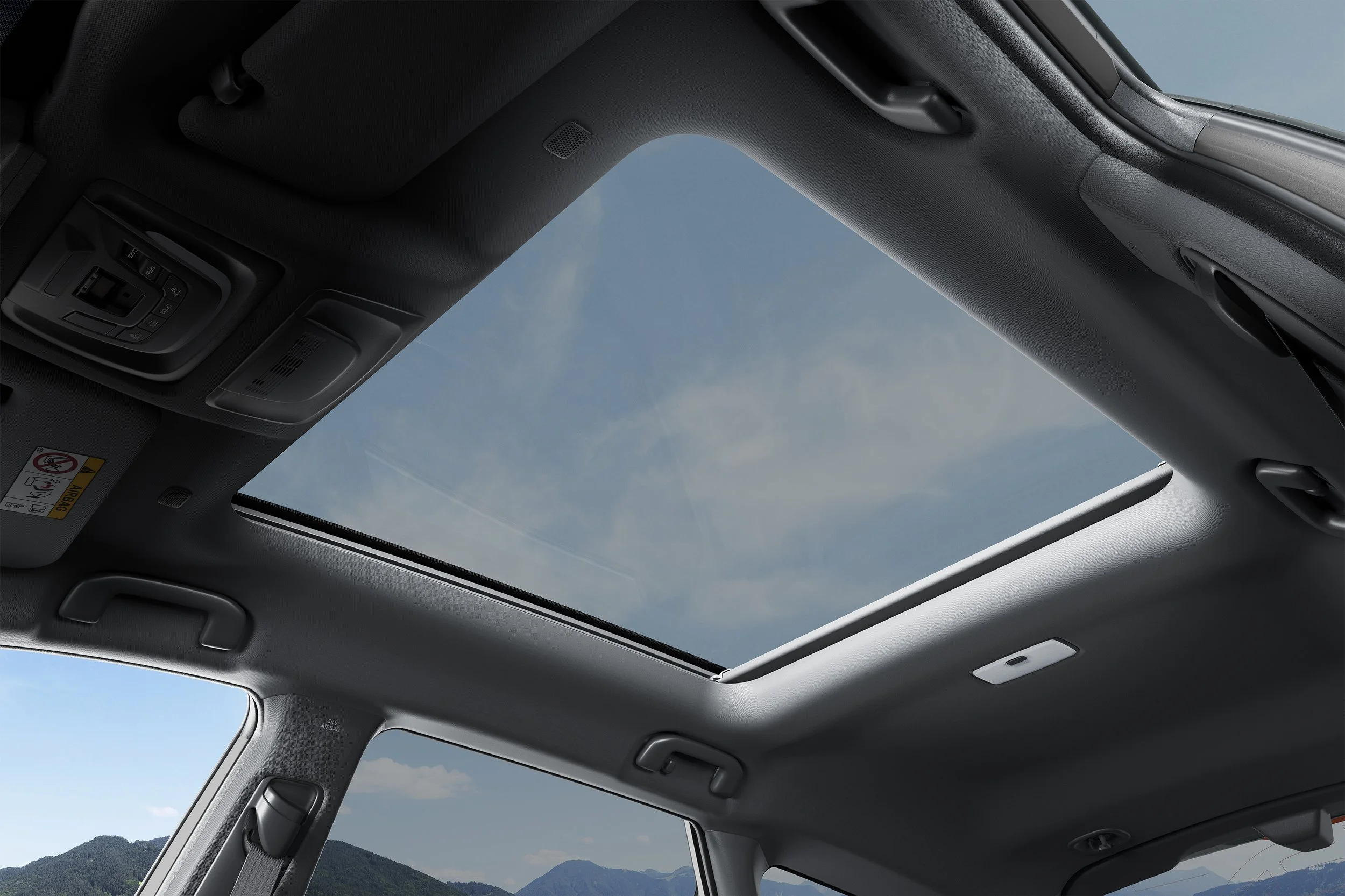 Utsikt gjennom takhimmelen av en bil med takvindu, med fjell og blå himmel utenfor.