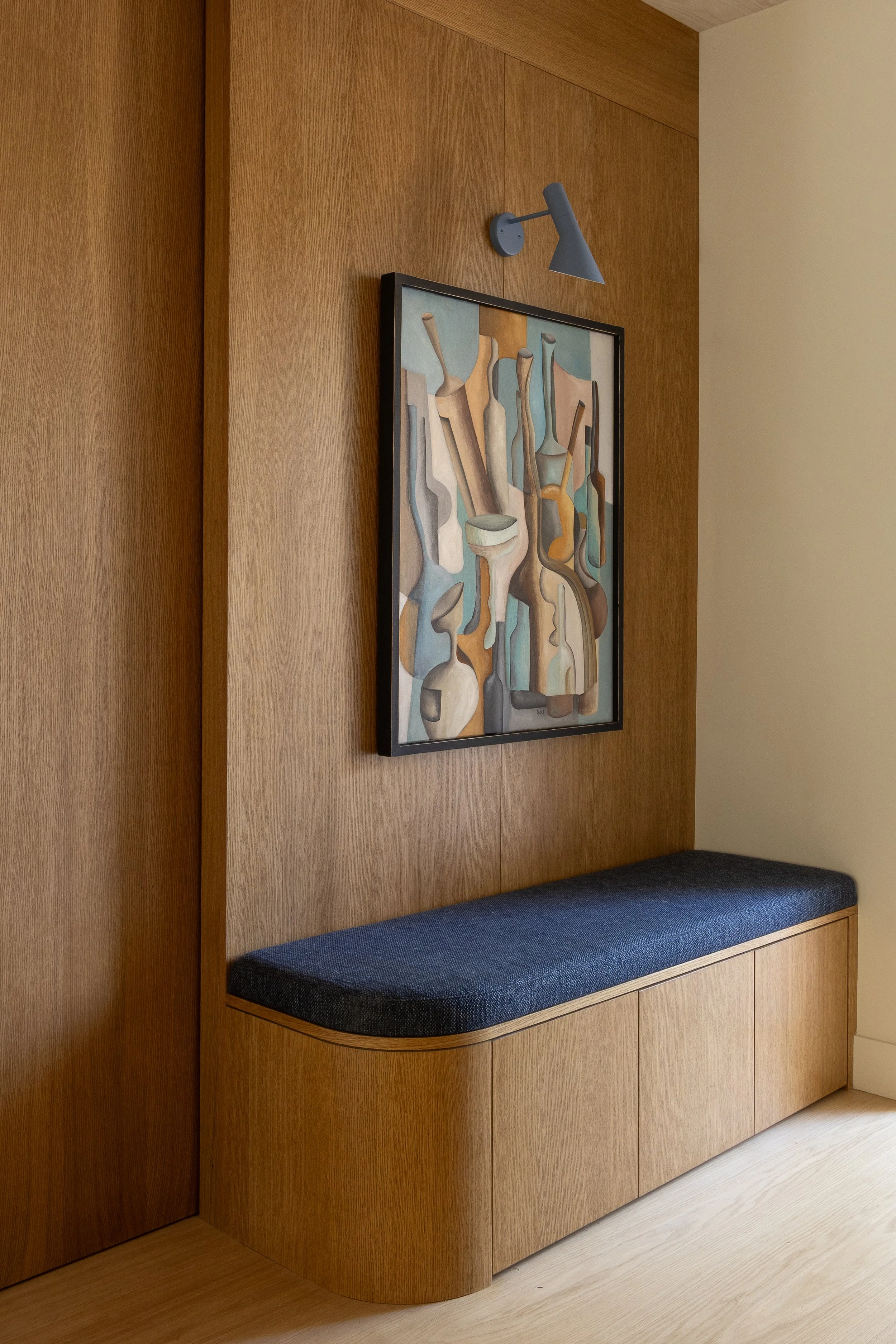 Bespoke oak hallway bench by ALL & NXTHING, with blue upholstery, curved joinery, oak wall panelling and framed abstract artwork.