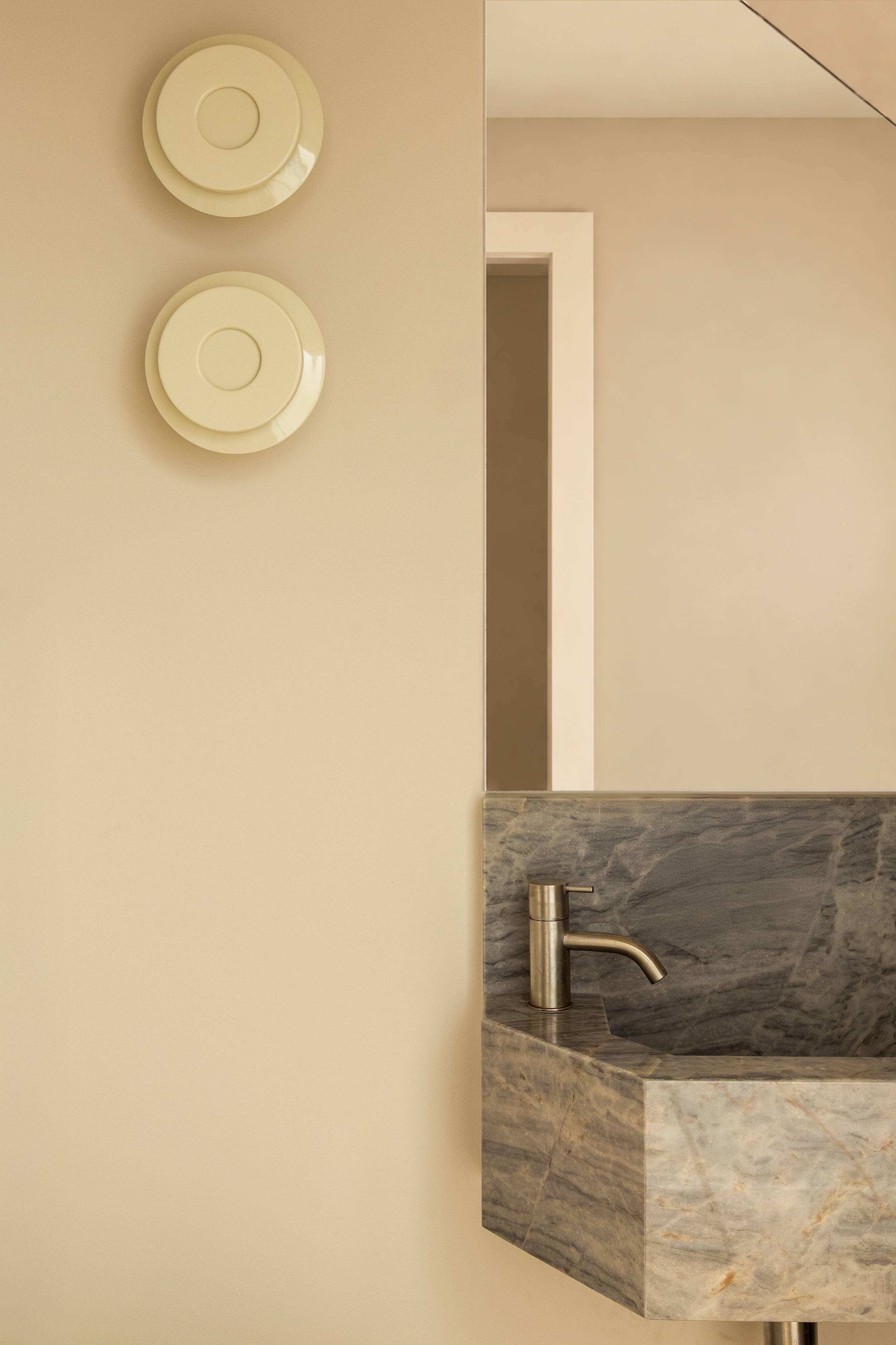 Cloakroom in Islington by ALL & NXTHING, featuring a sculptural marble basin, brass tap, bespoke frameless mirror and circular cream wall lights.
