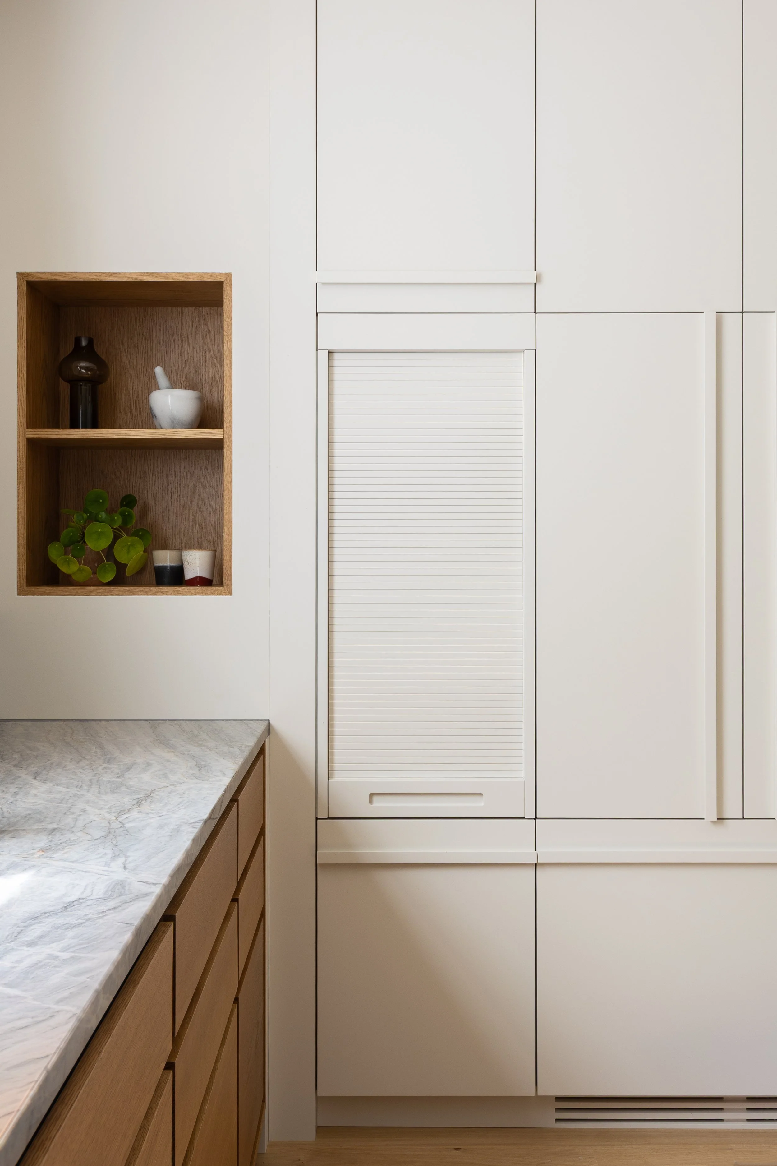 Bespoke kitchen coffee station in Islington by ALL & NXTHING, with an oak-lined appliance cupboard, cream tambour door, recessed shelving and marble worktop.