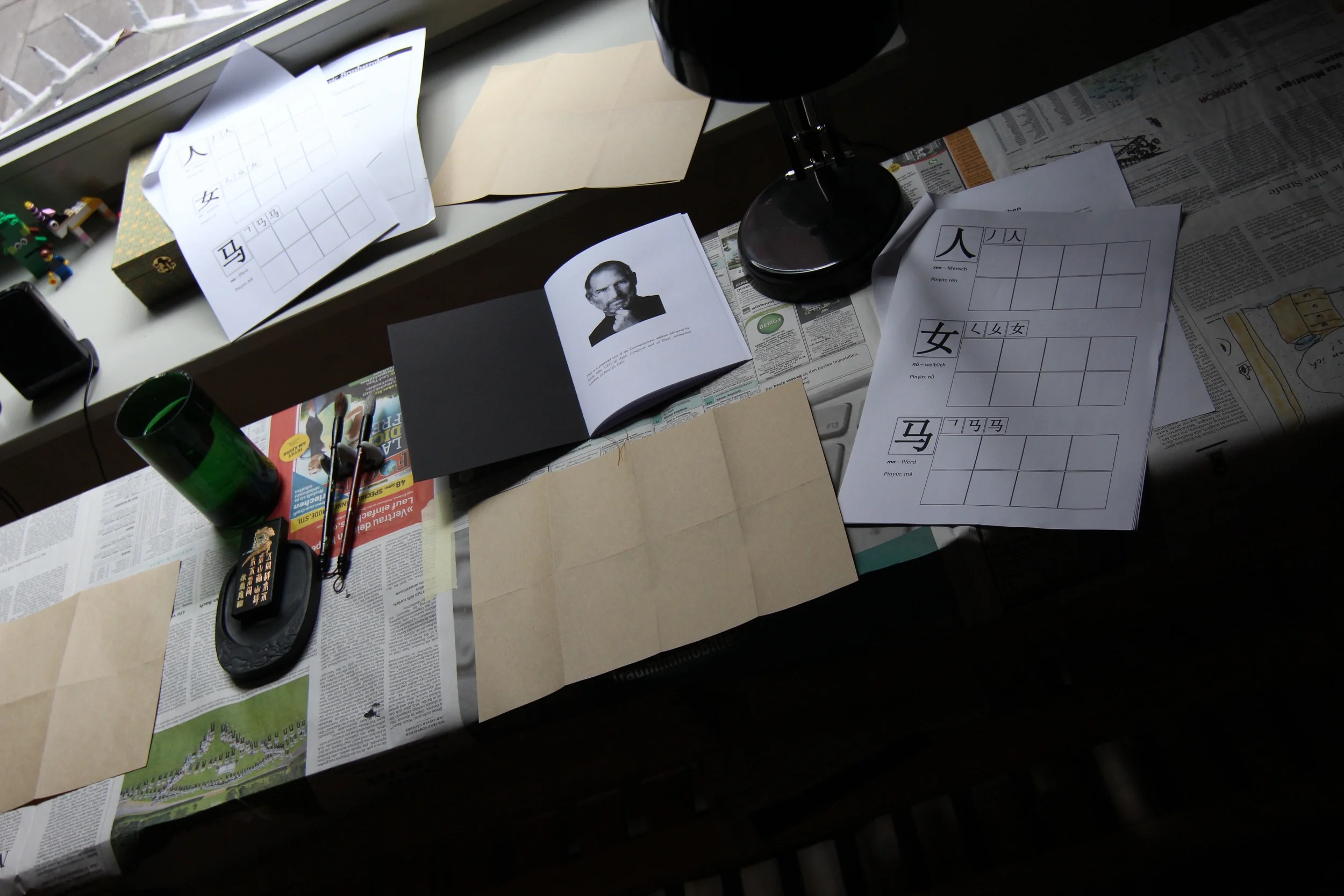 Eine Kalligrafie-Station mit Wasser, Tuschestein, Pinseln, Papier, chinesischen Schriftzeichen als Vorlage und ein Heft mit einer Rede von Steve Jobs, in der er erklärt, warum die Tatsache, dass er das College schmiss dazu führte, dass er Kalligrafie studierte, was wiederum das Design digitaler Devices prägte.