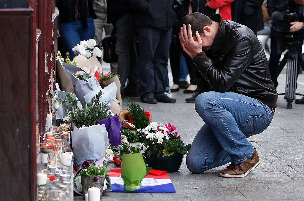  A man holds his head in his hands as he lays flowers in front of the Carillon cafe, in Paris, Saturday, Nov.14, 2015. French President Francois Hollande vowed to attack Islamic State without mercy as the jihadist group admitted responsibility Saturd