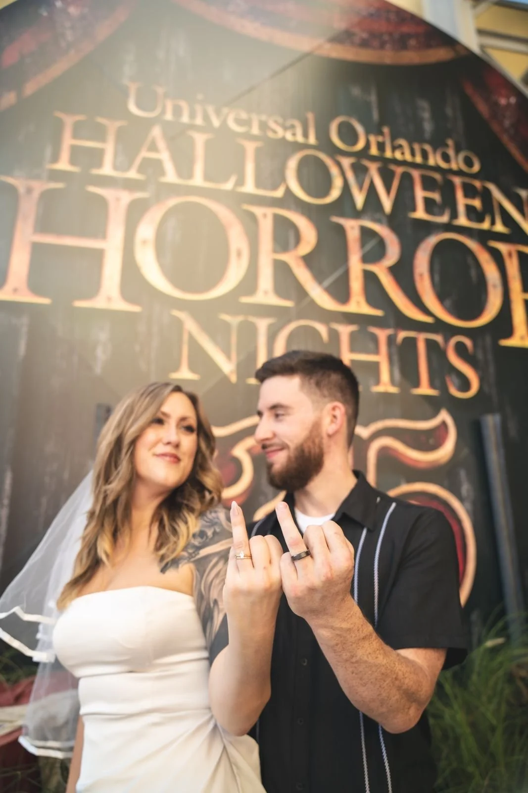 Couple showing off their wedding rings in front of the Universal Orlando Halloween Horror Nights sign