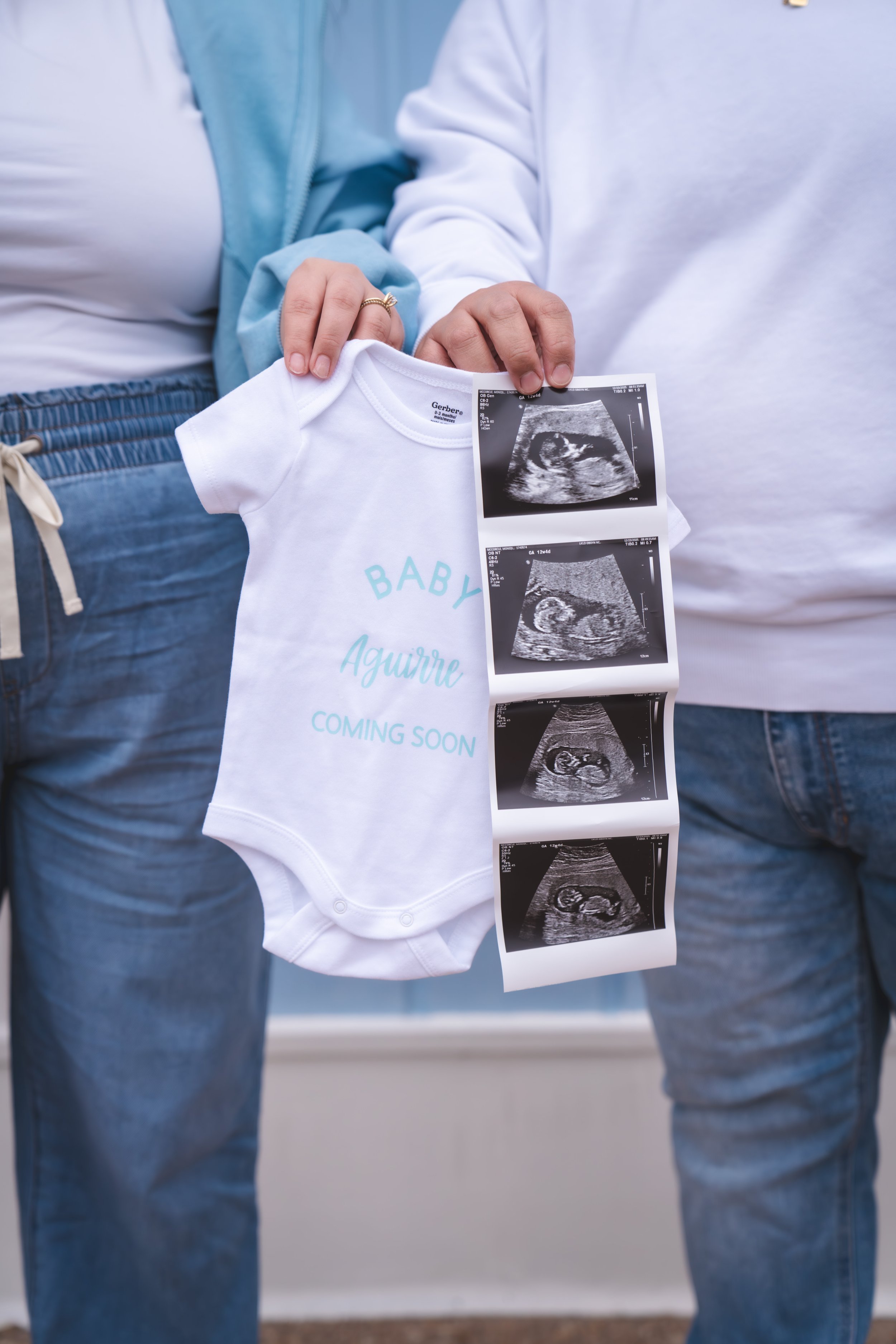A pregnant woman and a person holding ultrasound images with a white baby onesie, indicating an upcoming baby