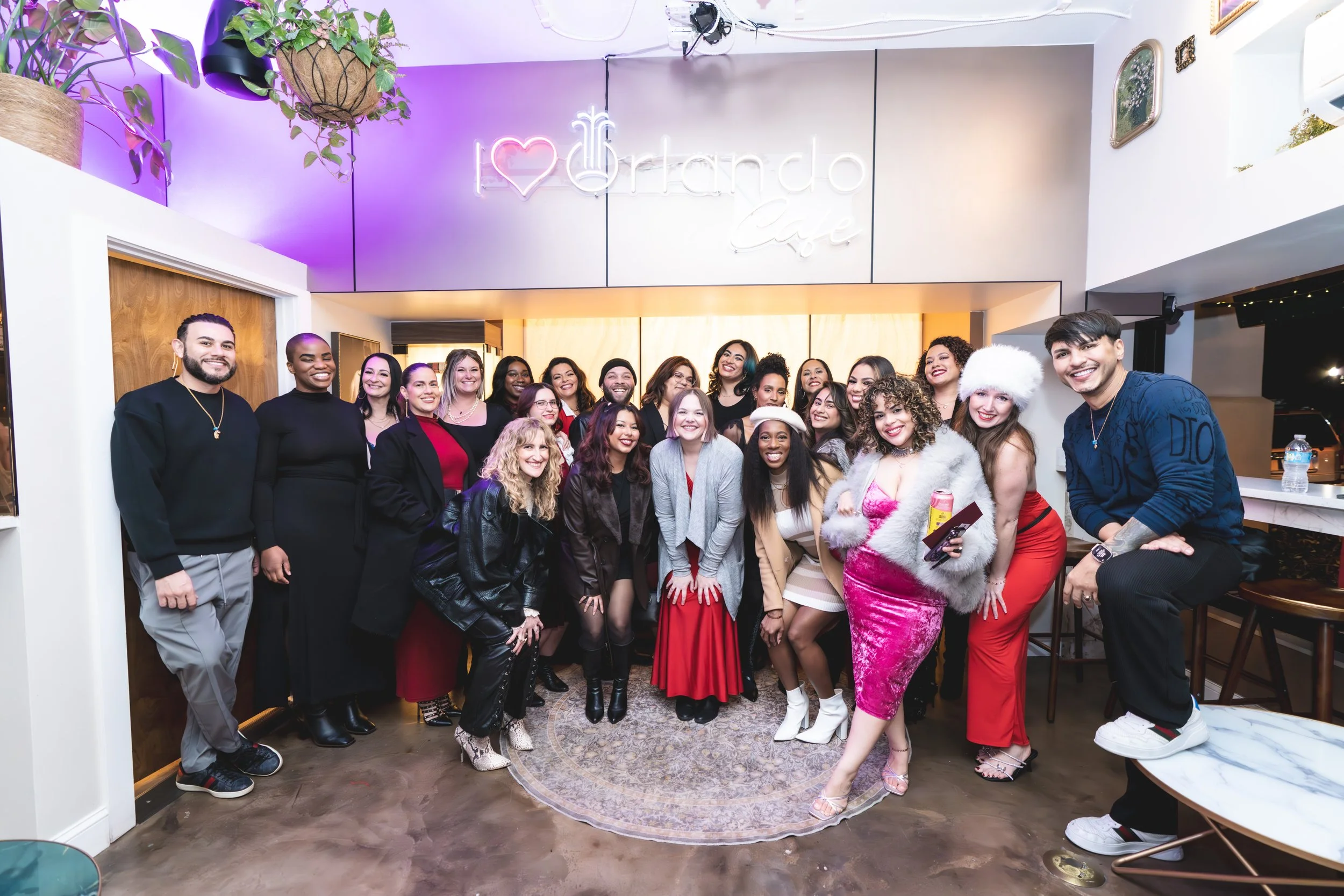 Group of people smiling and posing for a photo inside a cafe with a neon sign that reads 'I love Toronto Cafe', with plants and decorative items in the background.