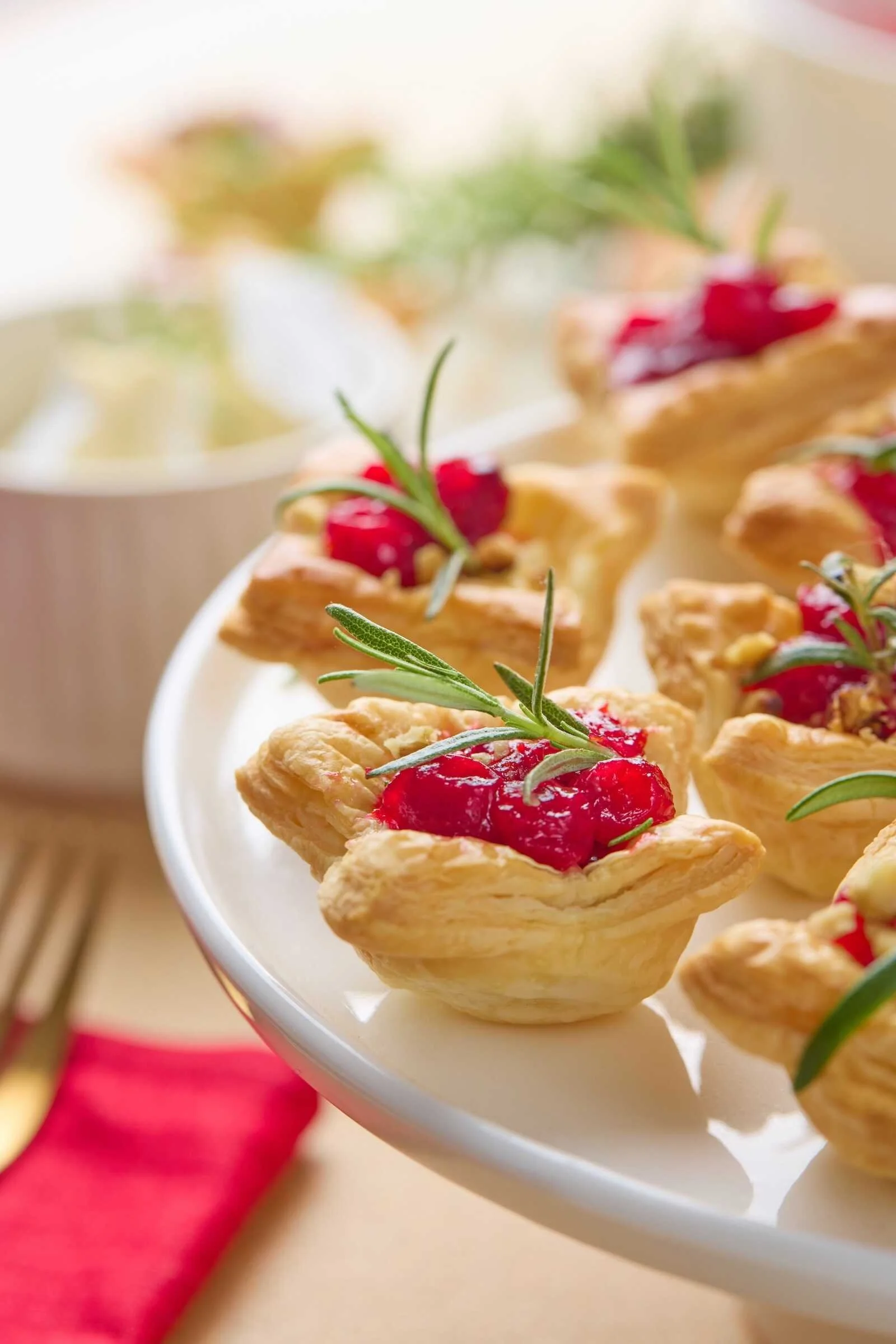 Close-up of Holiday Heaven Bites with flaky puff pastry, creamy Brie cheese, homemade cranberry topping, and fresh rosemary served on a festive holiday platter.