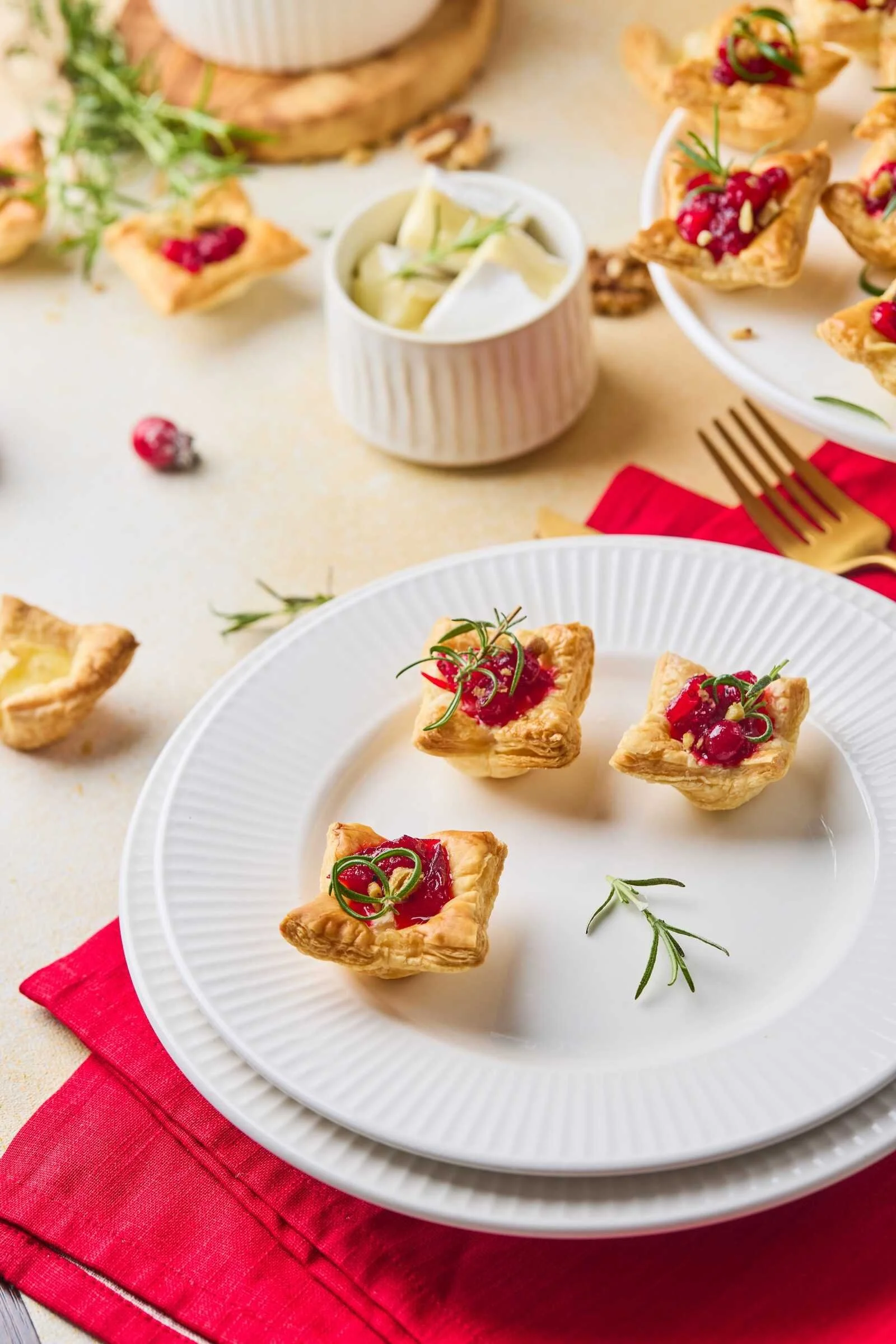 Holiday Heaven Bites served on a white plate with flaky puff pastry, creamy Brie cheese, homemade cranberry topping, and fresh rosemary for an easy holiday appetizer.