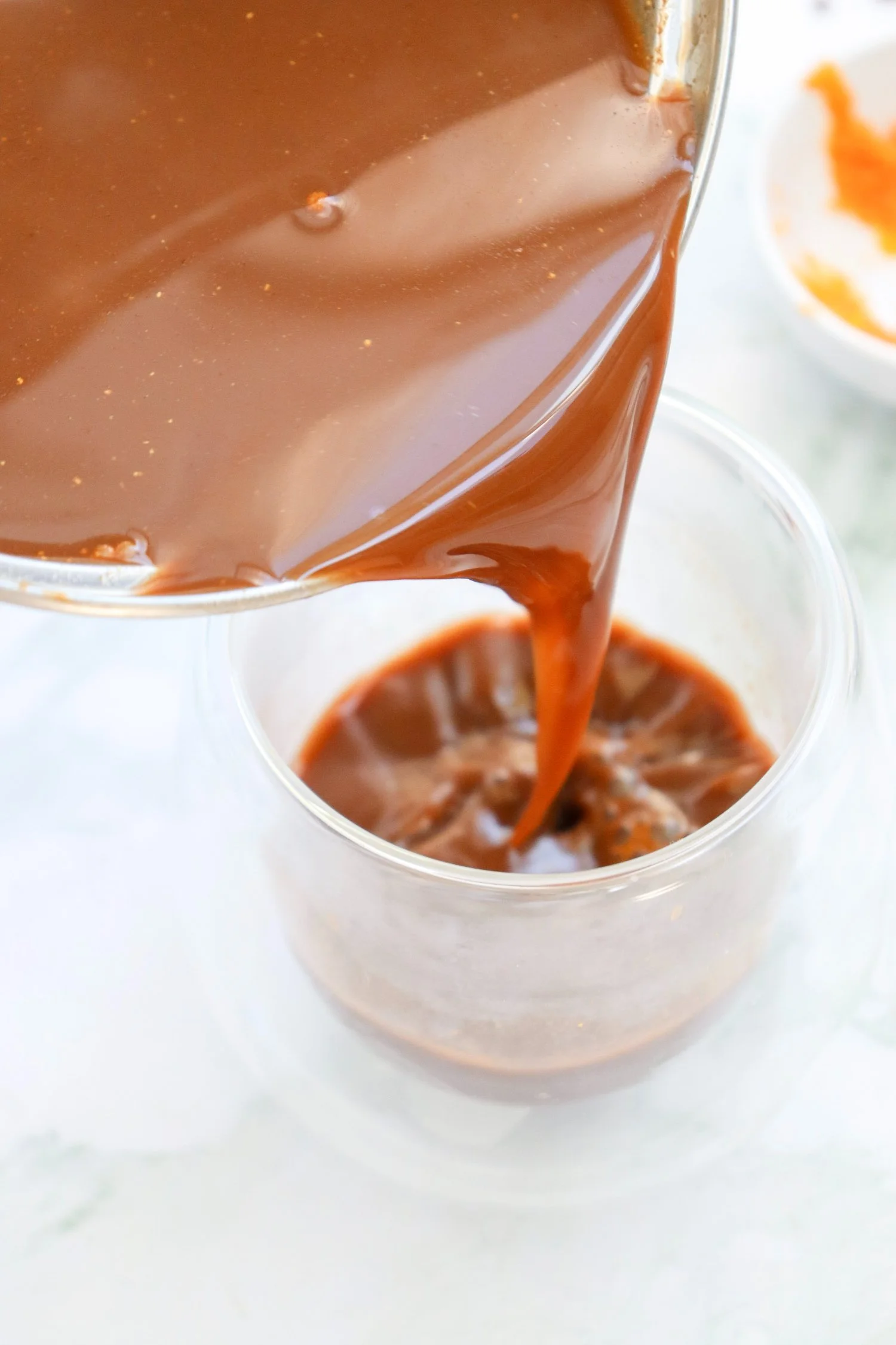 Pumpkin Spice Hot Chocolate being poured into a glass mug, showing the rich and creamy homemade fall chocolate drink.