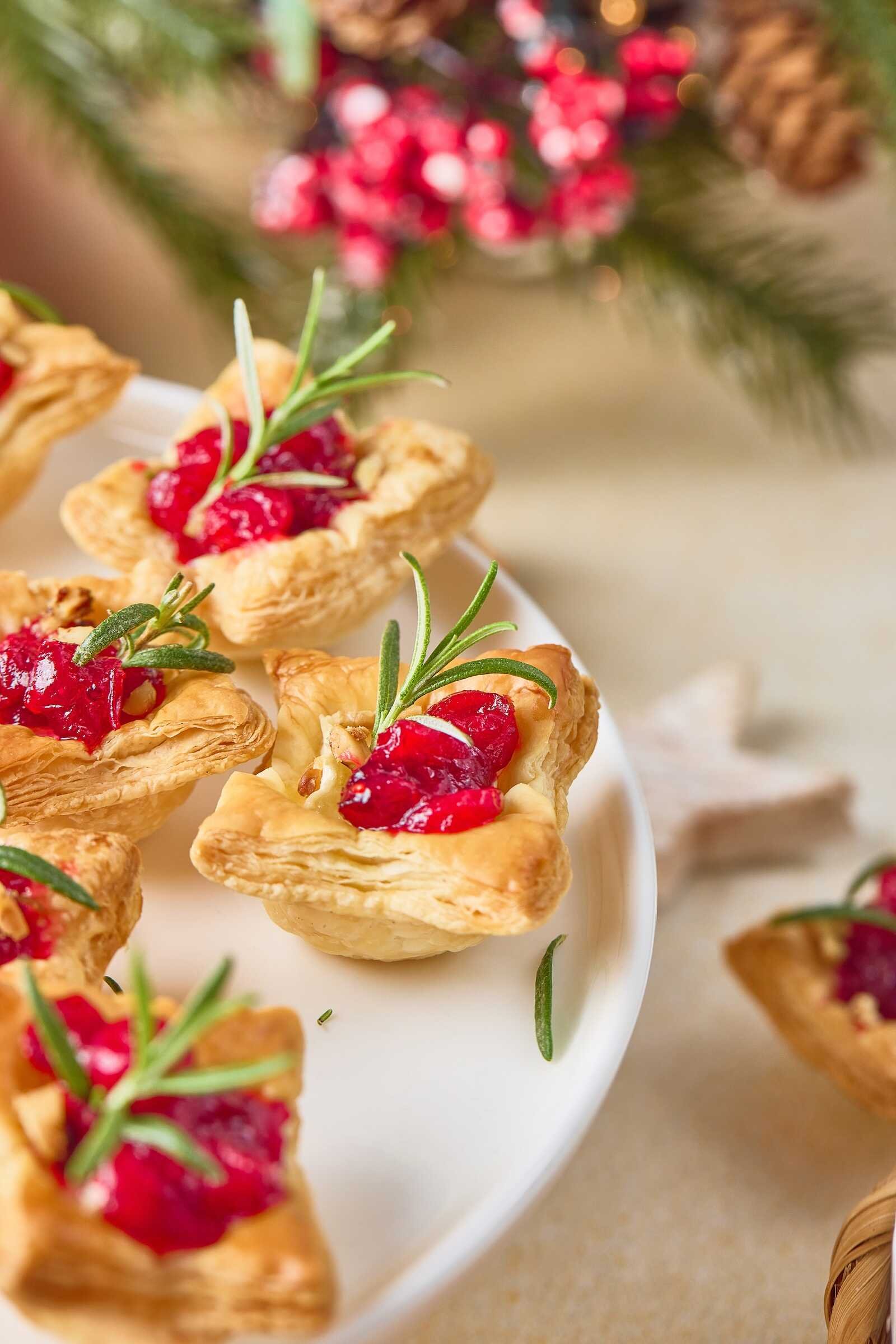 Holiday Heaven Bites with flaky puff pastry, melted Brie cheese, homemade cranberry topping, and fresh rosemary served on a festive holiday platter.