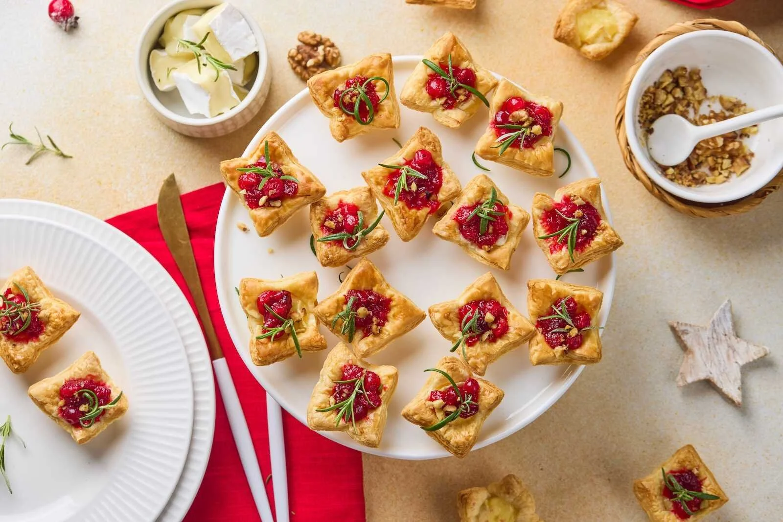 Overhead view of Holiday Heaven Bites with flaky puff pastry, creamy Brie cheese, homemade cranberry topping, chopped walnuts, and fresh rosemary served on a festive holiday platter.