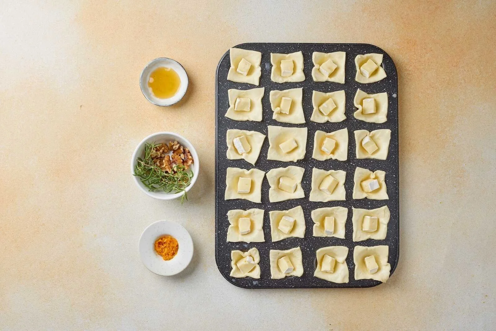 Egg-washed puff pastry cups filled with Brie cheese in a mini muffin pan, ready to bake into Holiday Heaven Bites with cranberry topping.